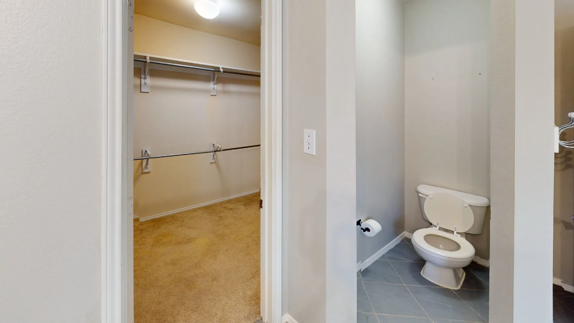 Walk-in storage area featuring wire shelving and carpet flooring, paired with a water closet on ceramic tile flooring