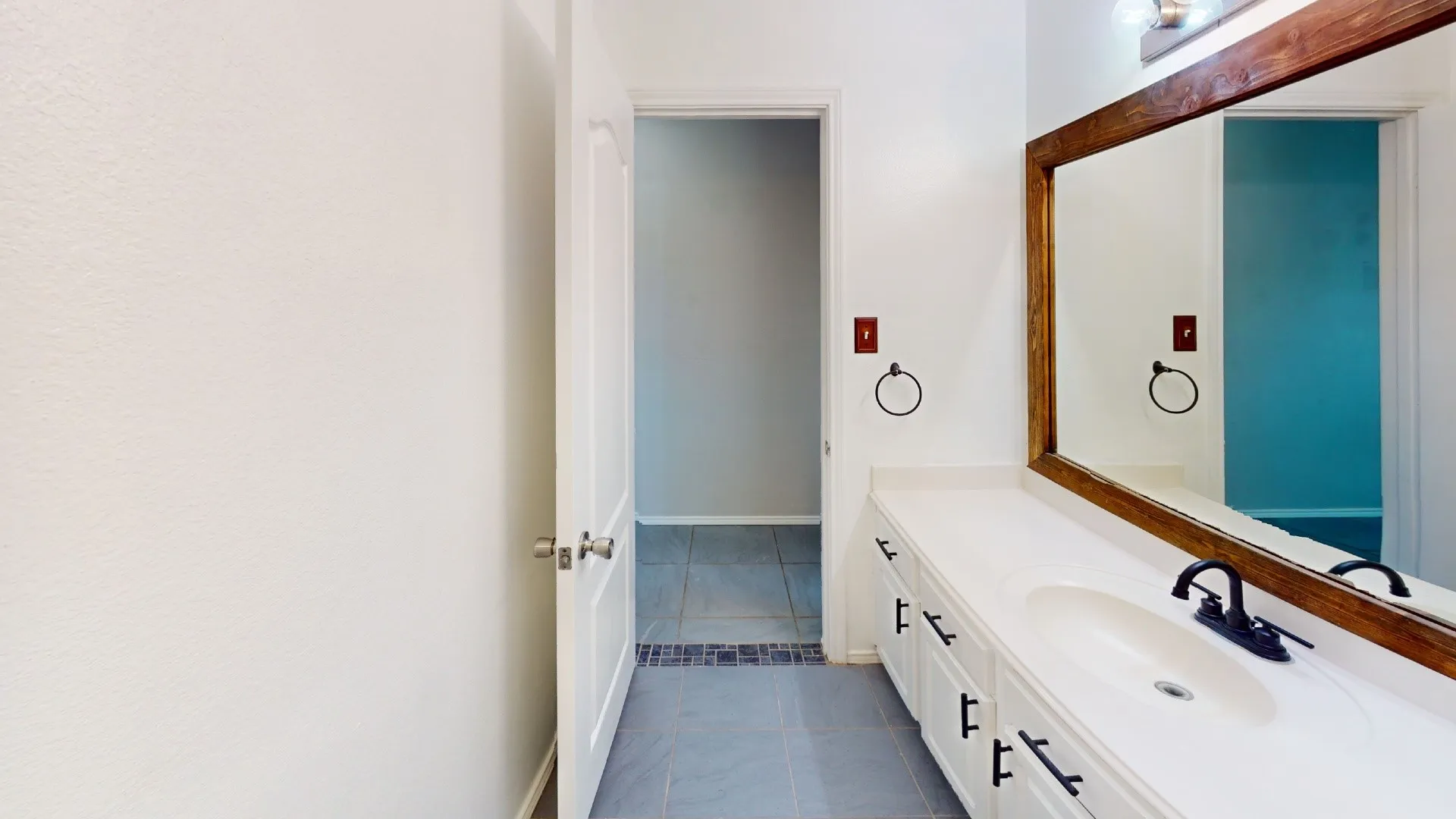 Bathroom vanity featuring white cabinetry, a solid surface countertop with integrated basin, matte black hardware, and a large wood-framed mirror