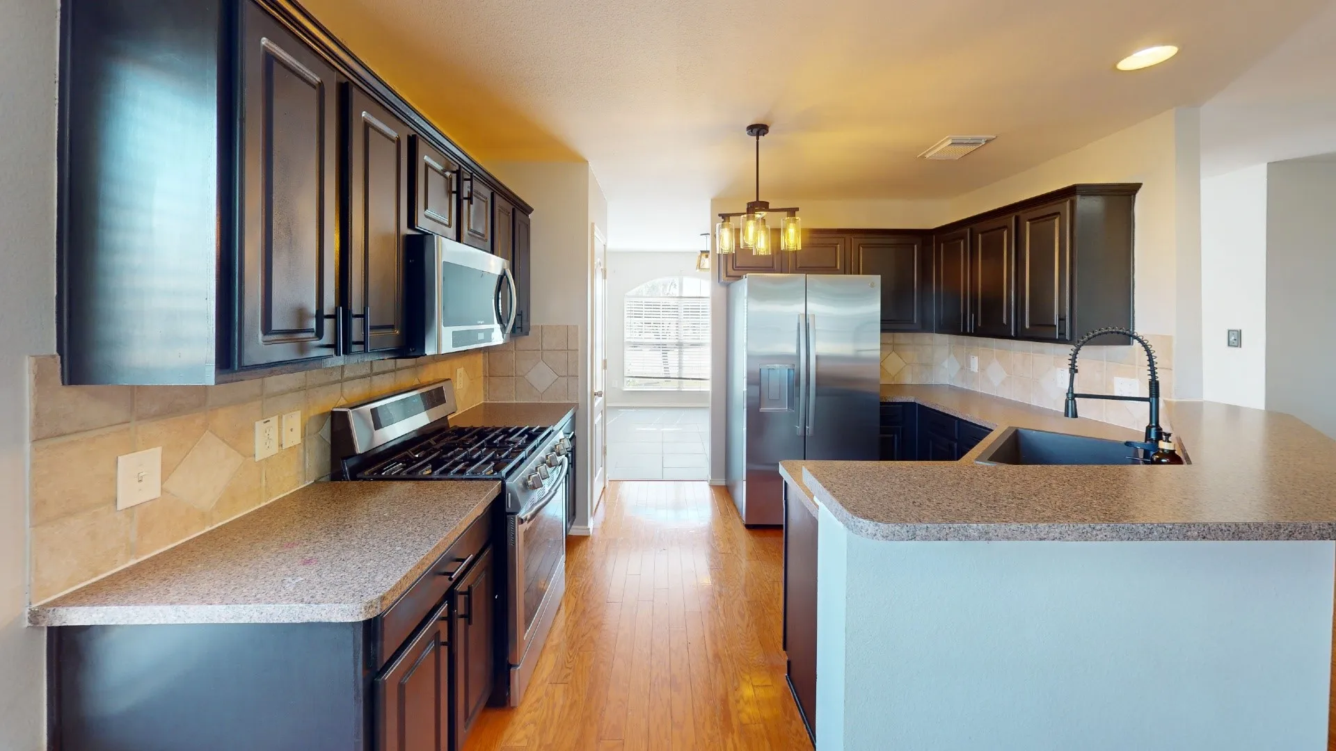 Kitchen featuring dark cabinetry, stone-finish countertops, stainless steel appliances, wood-finish flooring, and a neutral tile backsplash