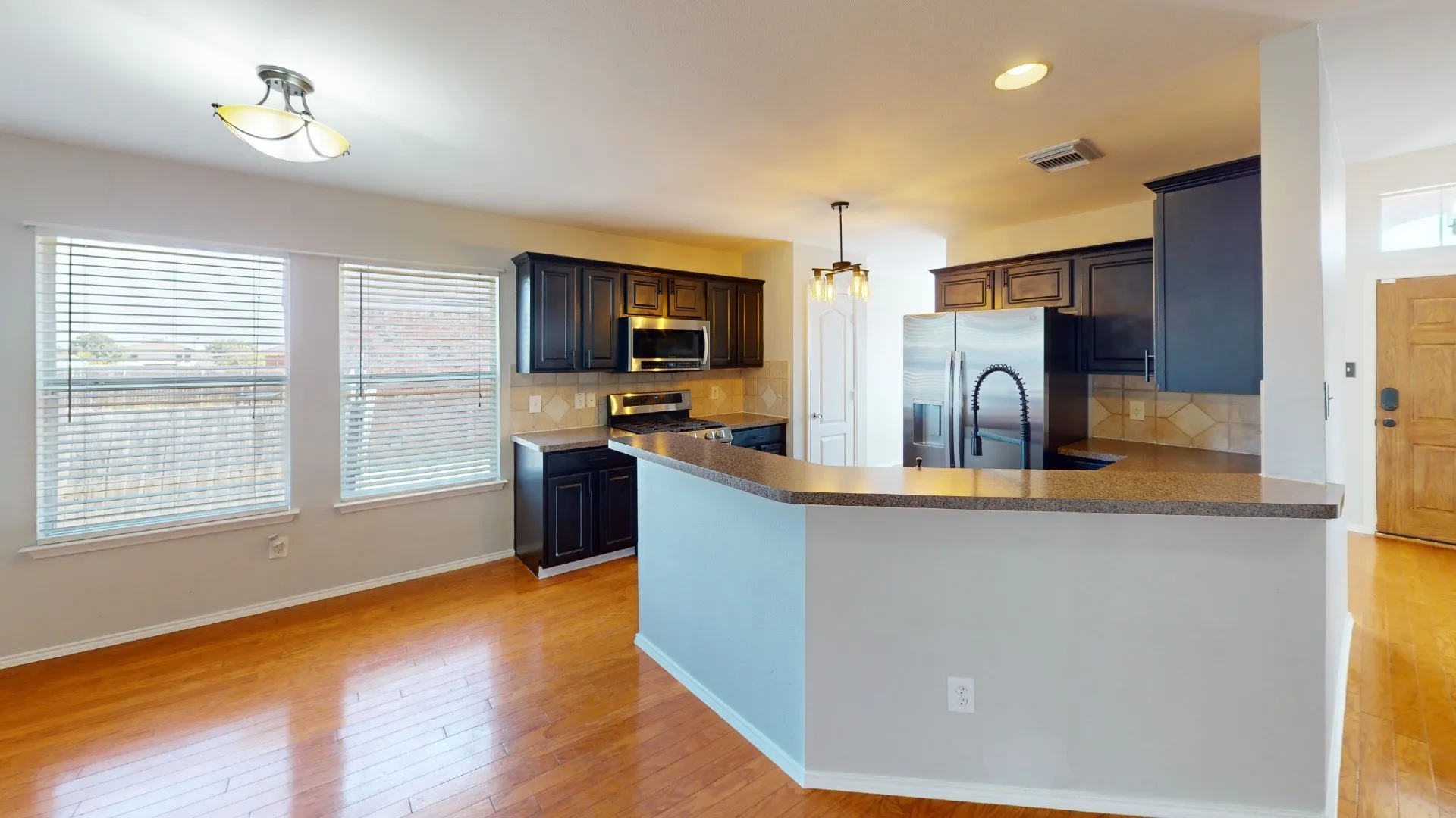 Kitchen featuring dark-finish cabinetry, an expansive breakfast bar, stainless steel appliances, tile backsplash, and wood-finish flooring