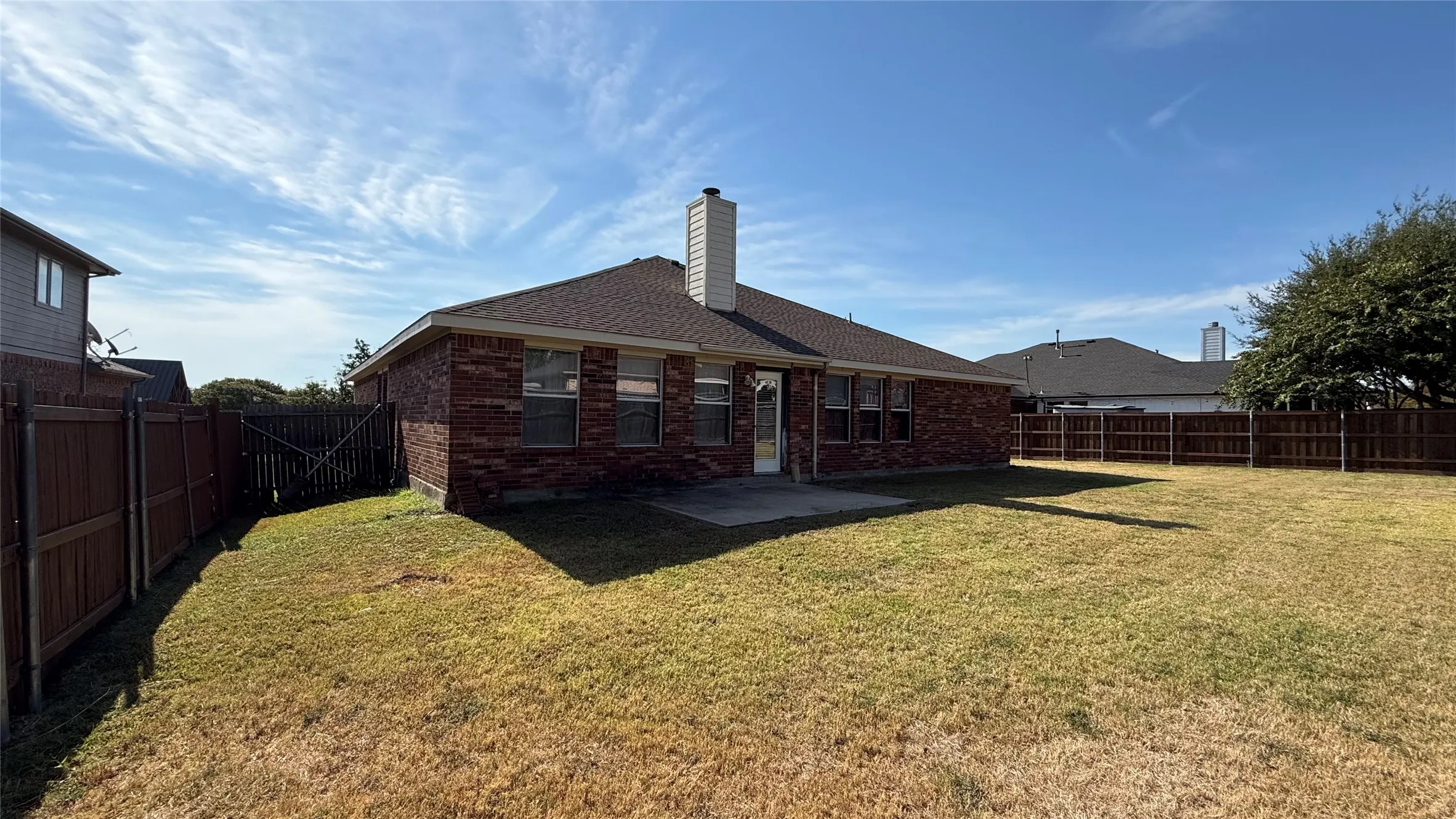 Backyard featuring a brick exterior, shingled roof, exterior chimney, concrete patio, and full wood perimeter fencing