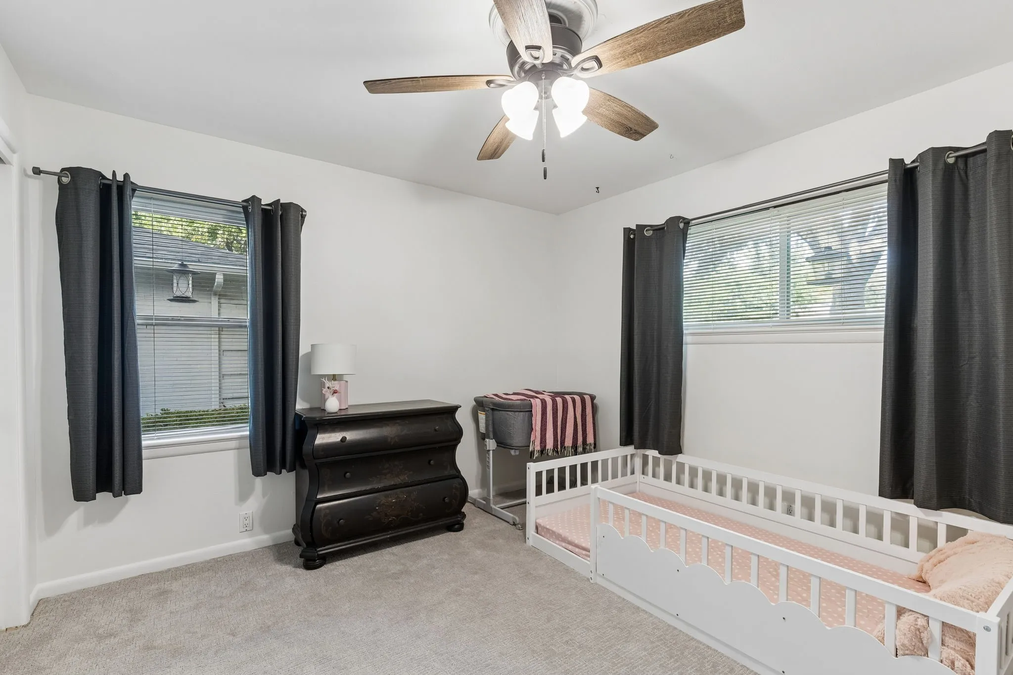 Neutral-toned wall-to-wall carpeting, dual-aspect windows, and a ceiling-mounted light fixture with a multi-blade fan