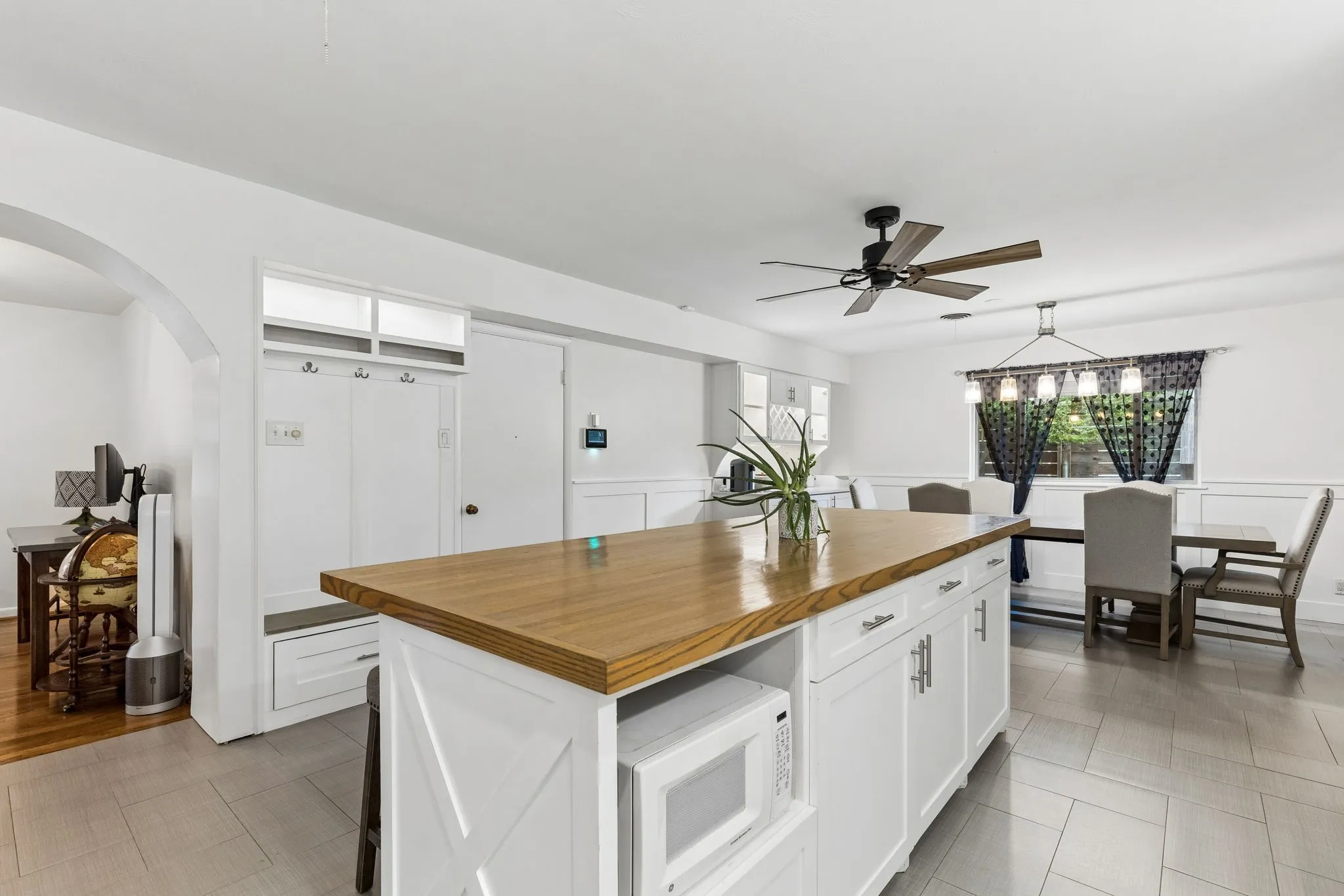Center island featuring a wood-finish countertop and built-in microwave, integrated mudroom storage cabinetry, ceiling-mounted fan, tile flooring, and wall paneling