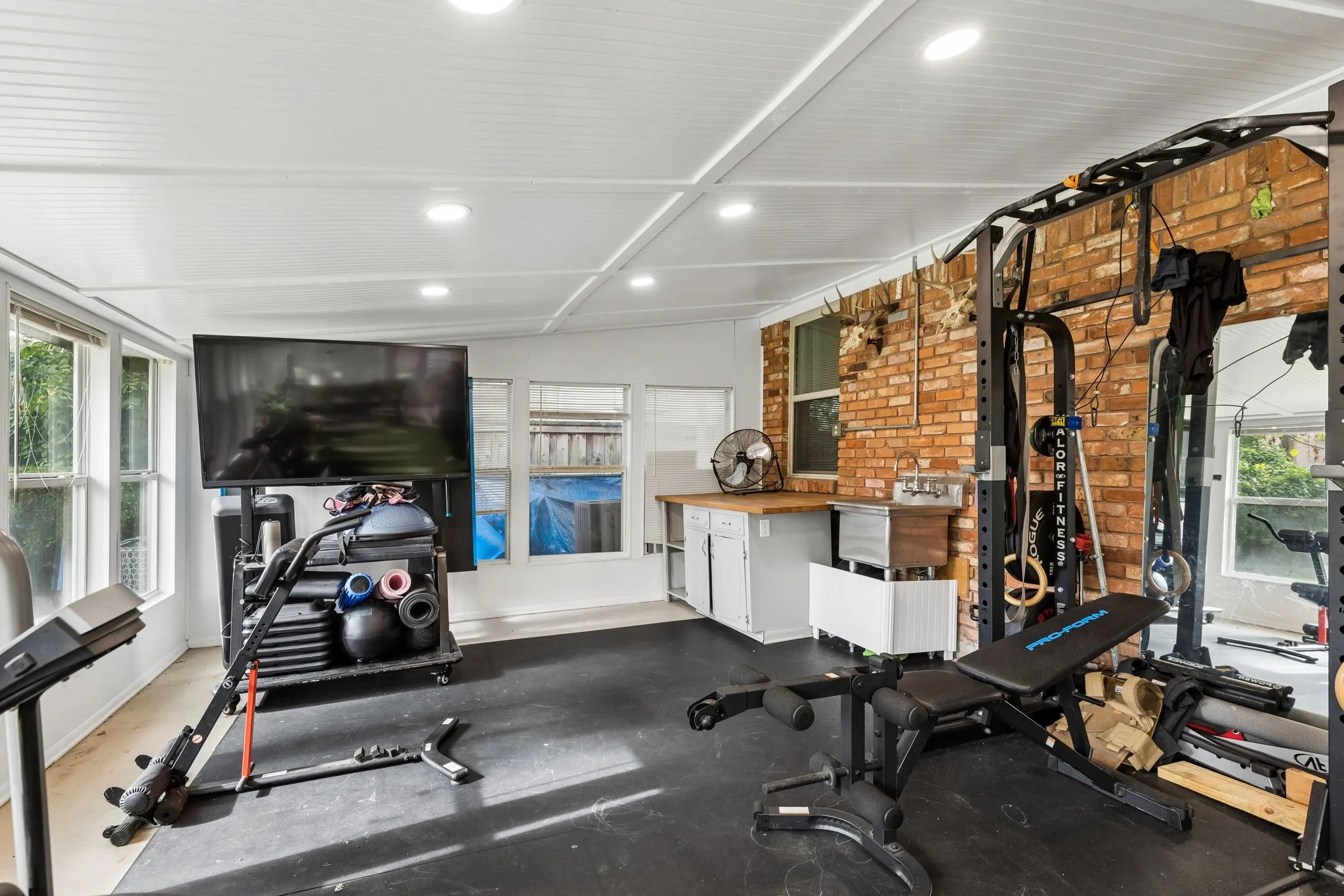 Enclosed sunroom featuring a brick accent wall, recessed lighting, beadboard-style ceiling, multi-pane windows, and custom built-in cabinetry with a wood countertop