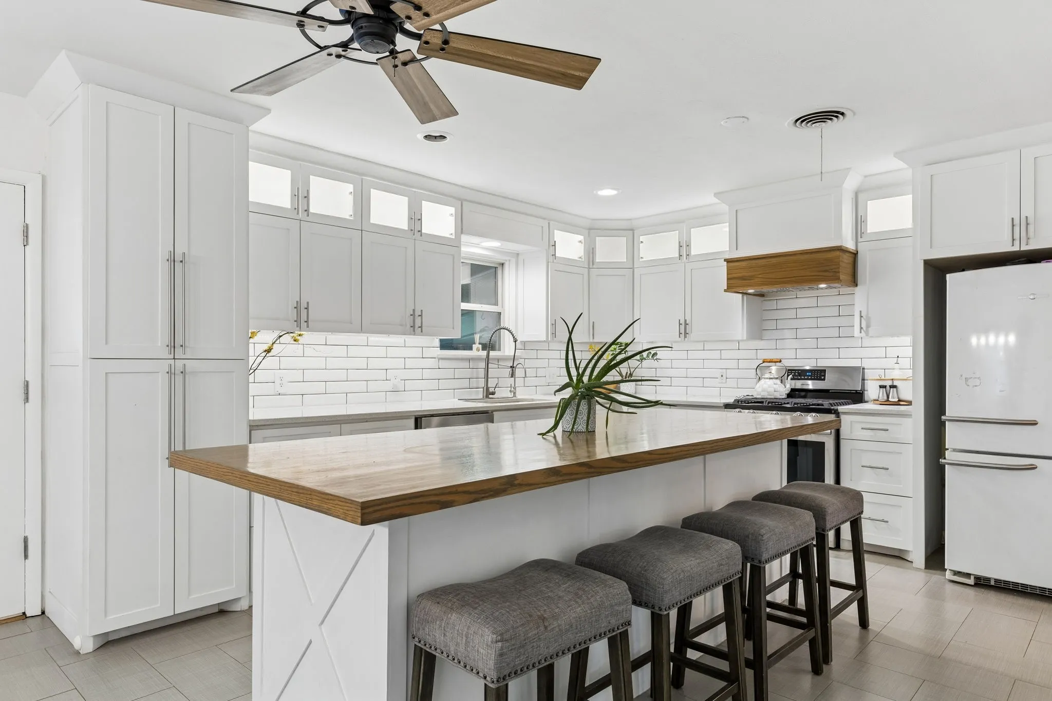 Kitchen featuring white shaker cabinetry, a wood-topped island, white subway tile backsplash, crown molding, and a wood-accented range hood
