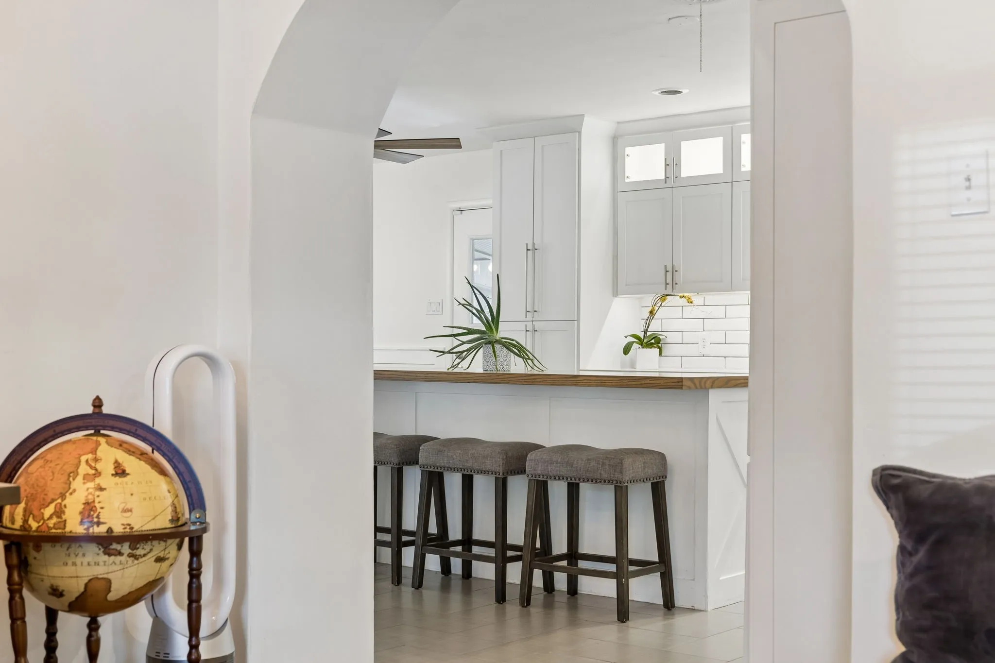 Arched entryway featuring white cabinetry, subway tile backsplash, and a breakfast bar with a wooden countertop
