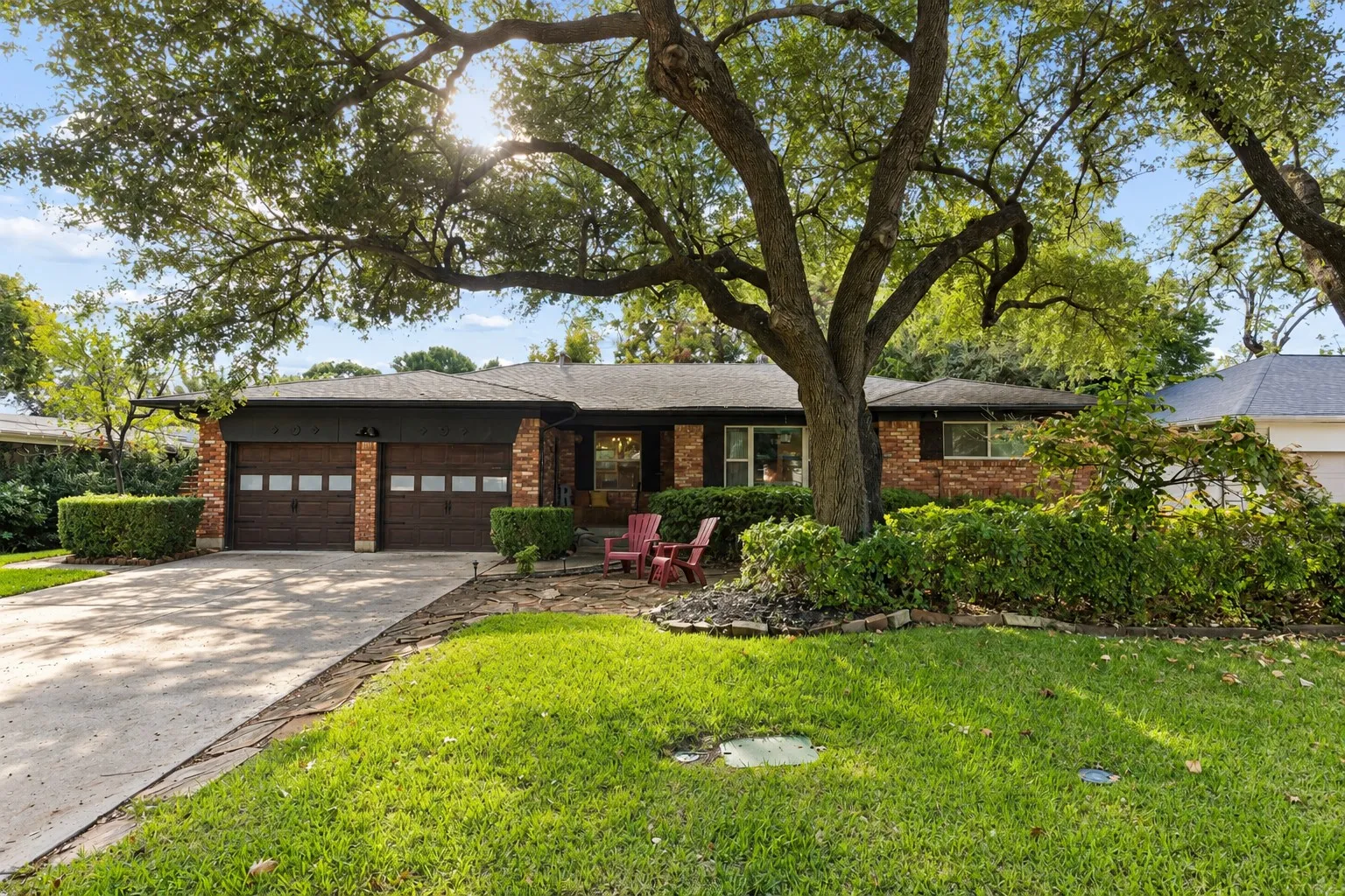Brick exterior residence featuring a two-car garage with glass-panel doors, stone-paved walkway, concrete driveway, and mature canopy trees