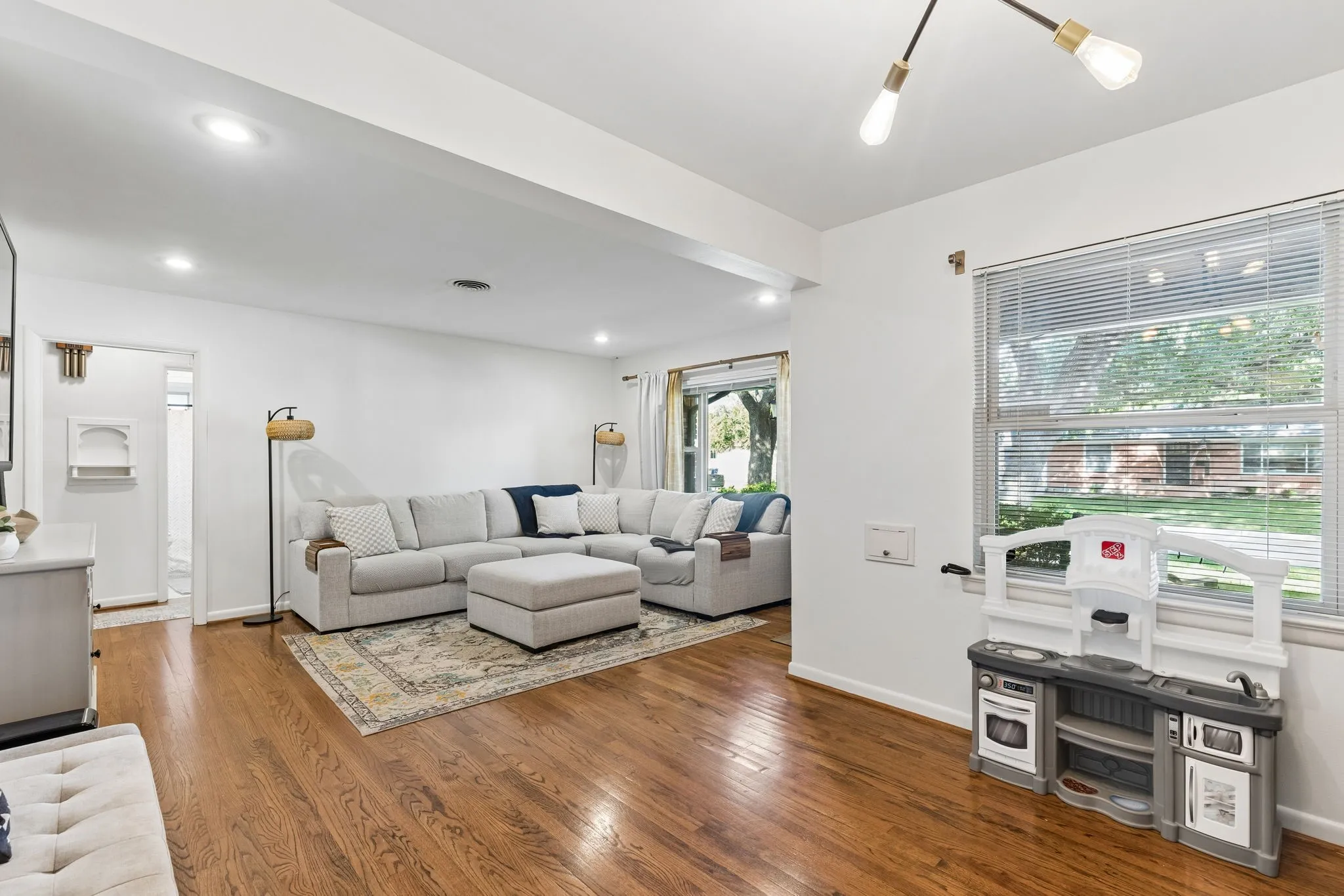 Living area featuring wood-finish flooring, recessed lighting, a modern multi-arm ceiling fixture, and large windows with horizontal blinds