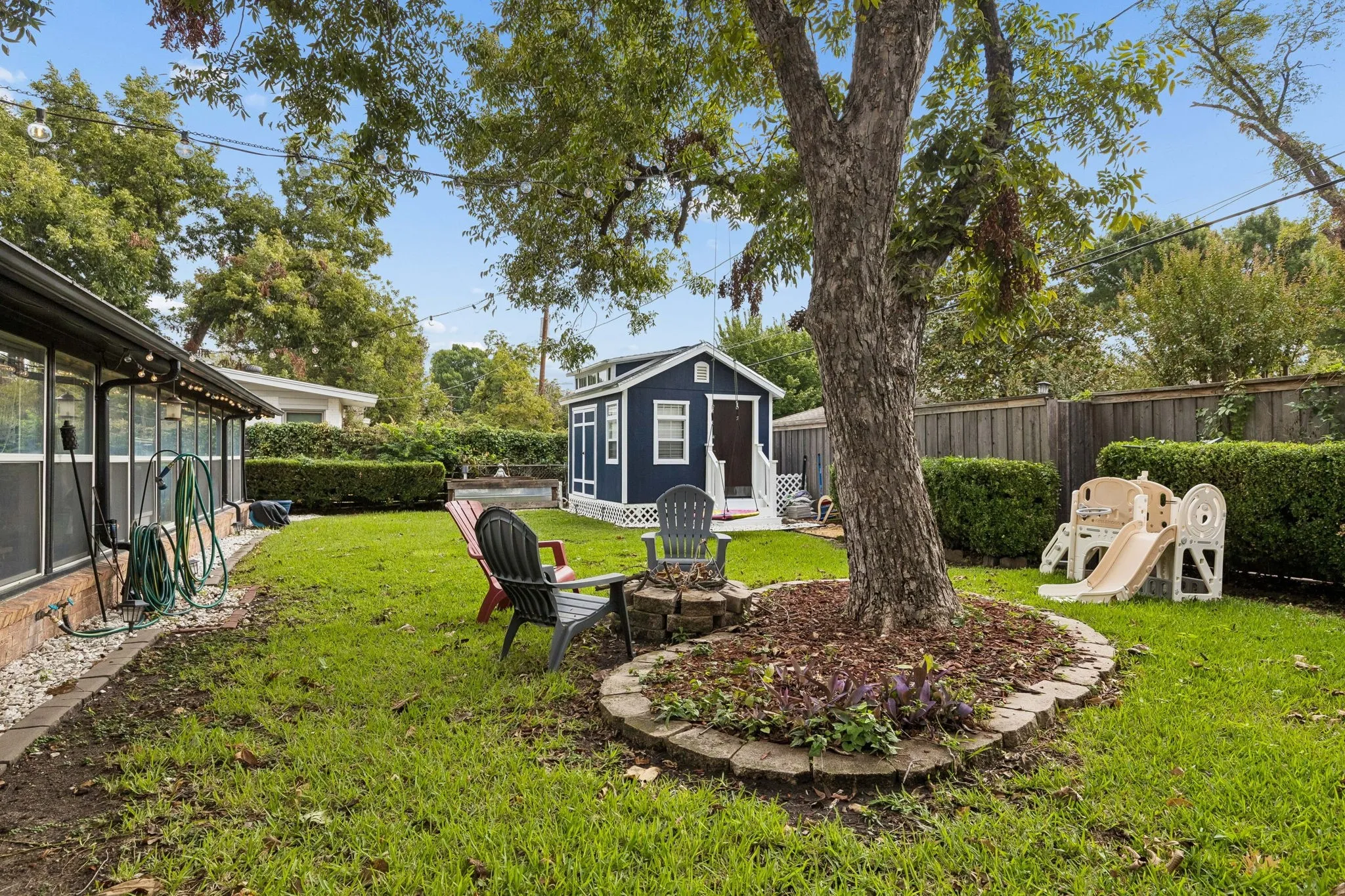 Backyard featuring a detached accessory structure, stone-bordered landscaping, mature shade tree, and wood-slat perimeter fencing