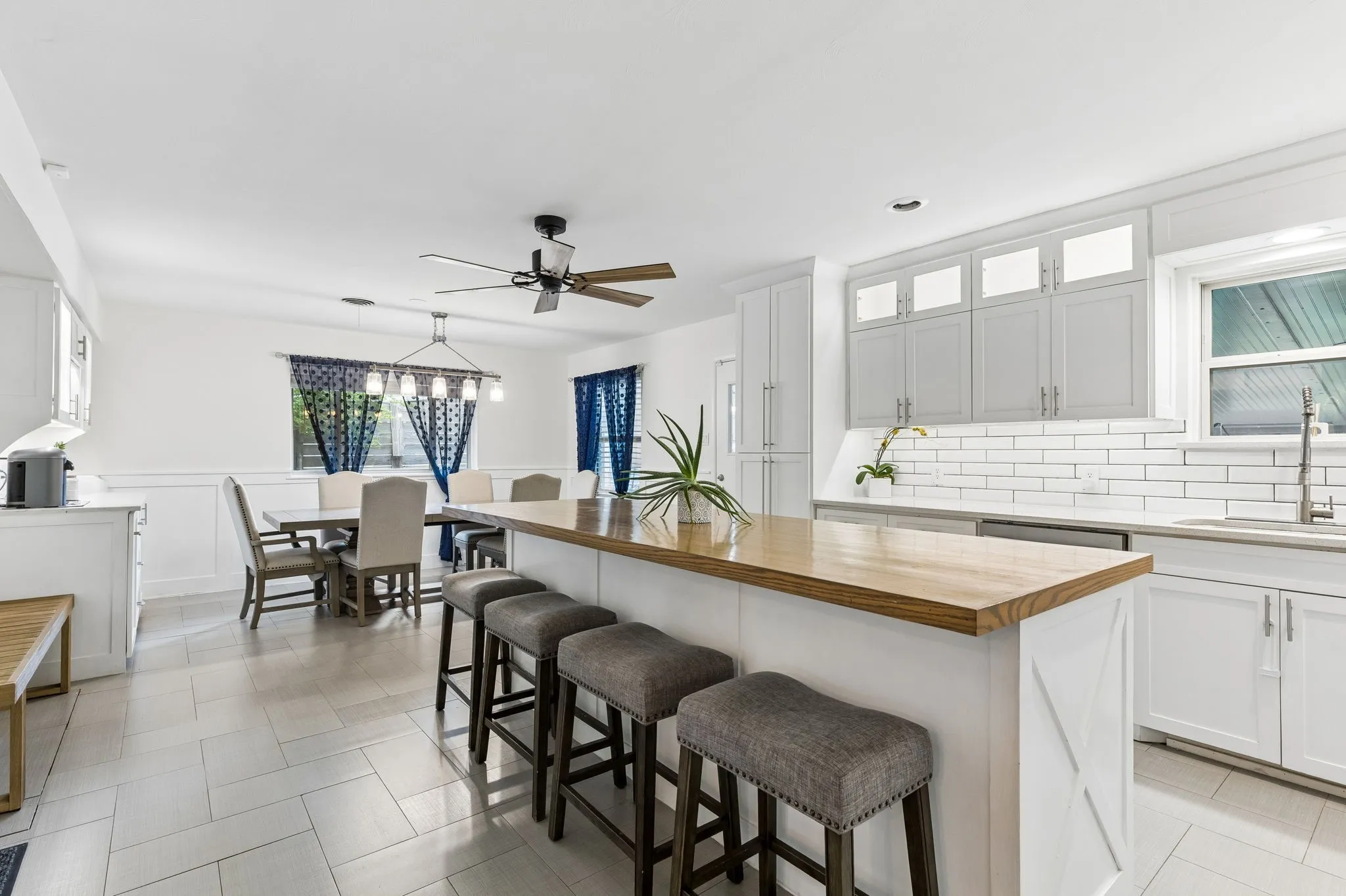 Kitchen featuring white shaker-style cabinetry with upper transom glass doors, wood-finish island countertop, white subway tile backsplash, and ceramic tile flooring