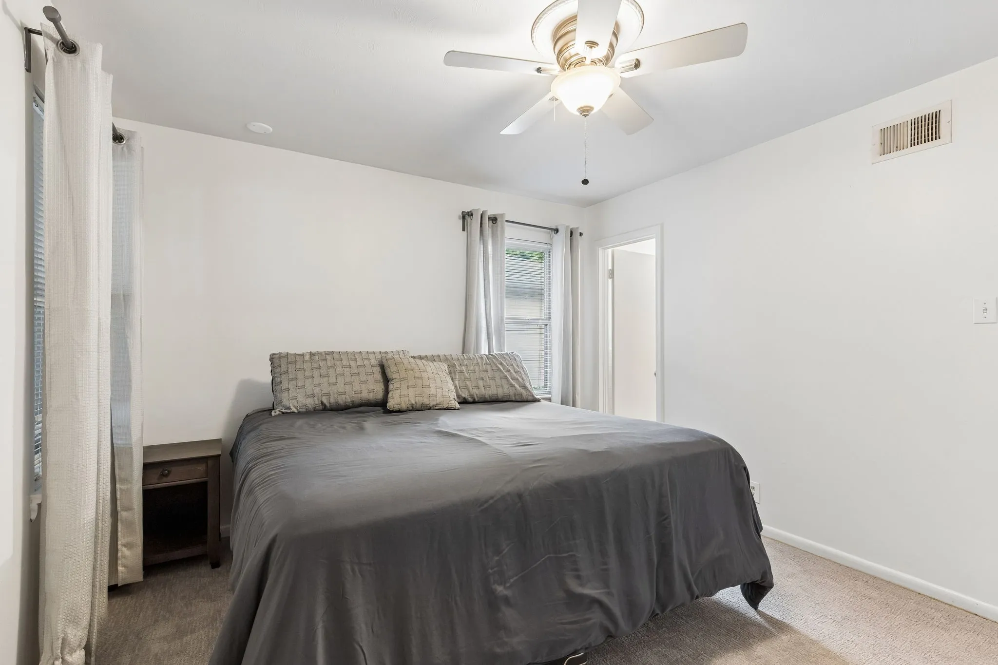 Neutral-toned interior space featuring wall-to-wall carpeting, multiple windows, and a ceiling-mounted light fixture with a five-blade fan