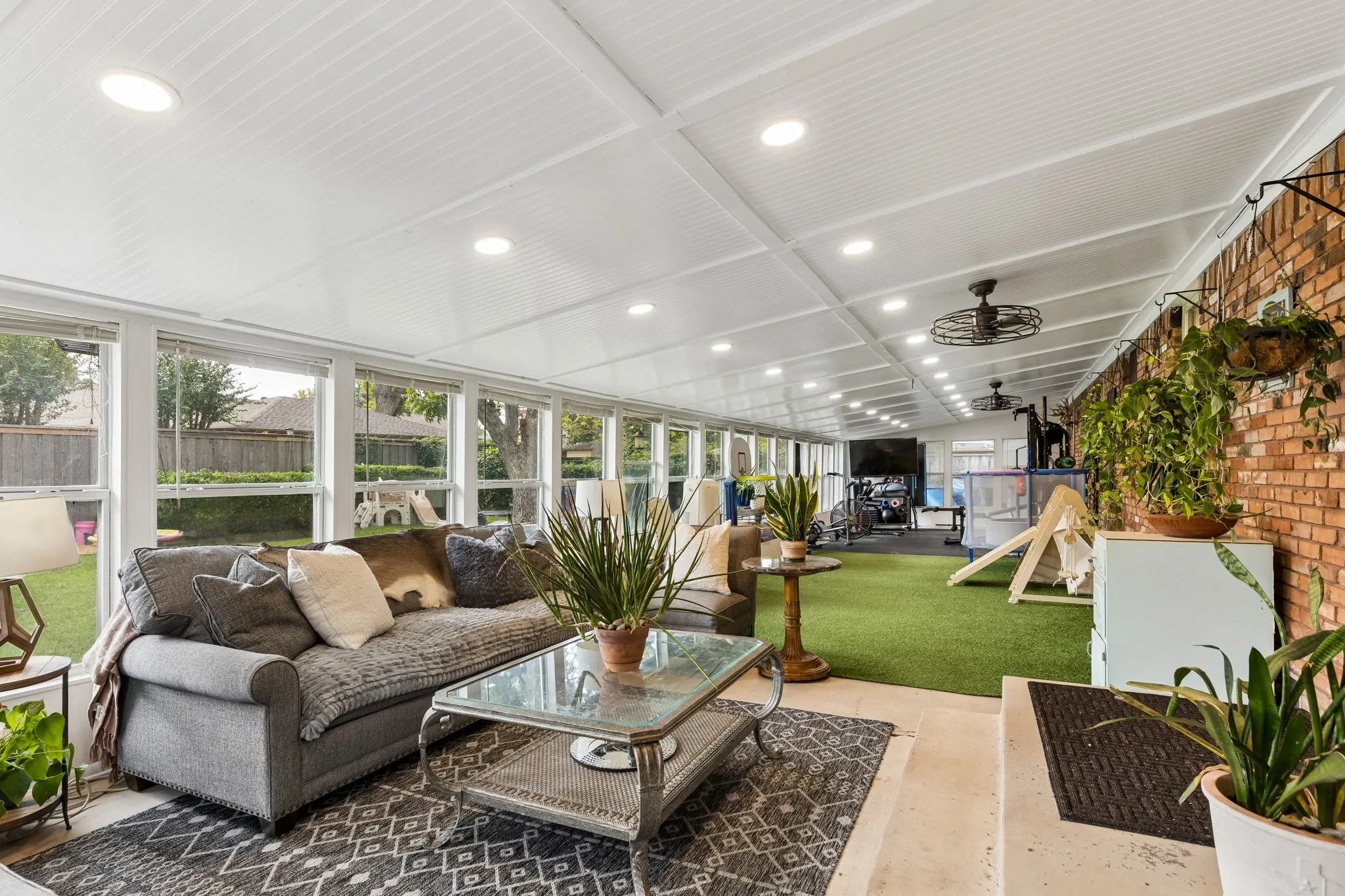 Enclosed patio featuring extensive window walls, a beadboard ceiling with recessed lighting, an exposed brick wall, and artificial turf flooring