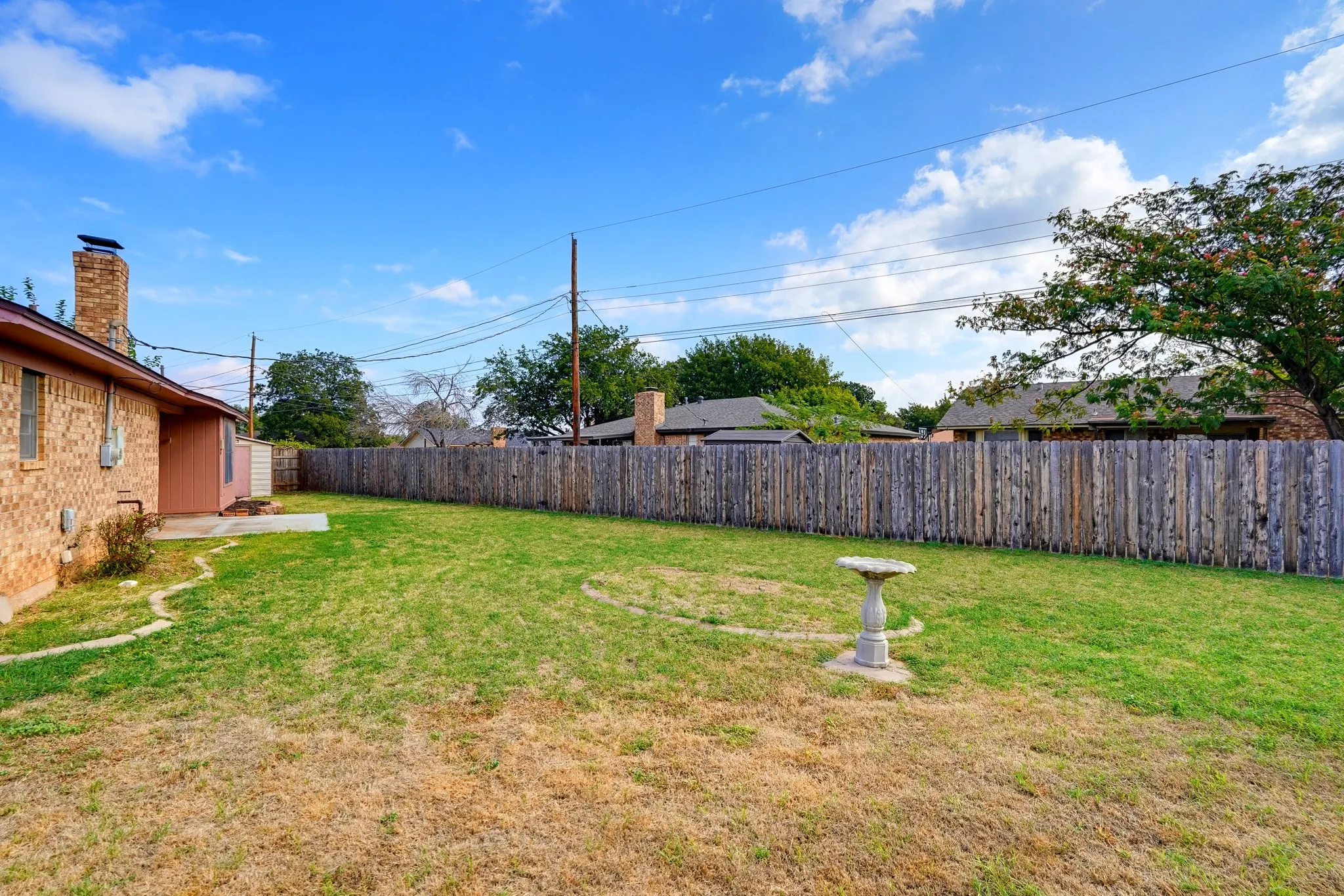 Room to roam, with a birdbath, a shed, and a wide stretch of grass behind a privacy fence.