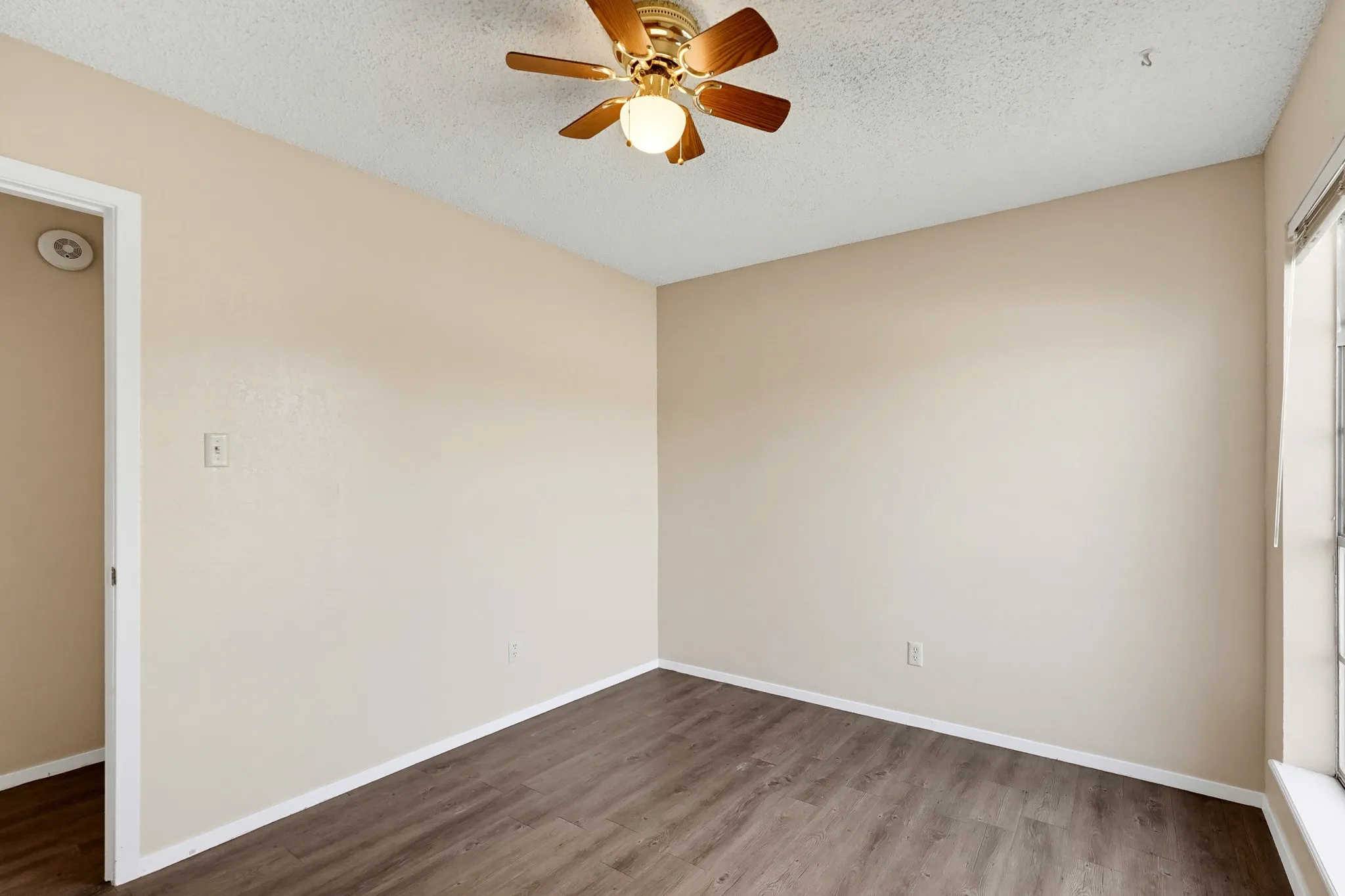 Soft neutral walls and a breezy fan overhead, ready for a bed, a desk, or both.