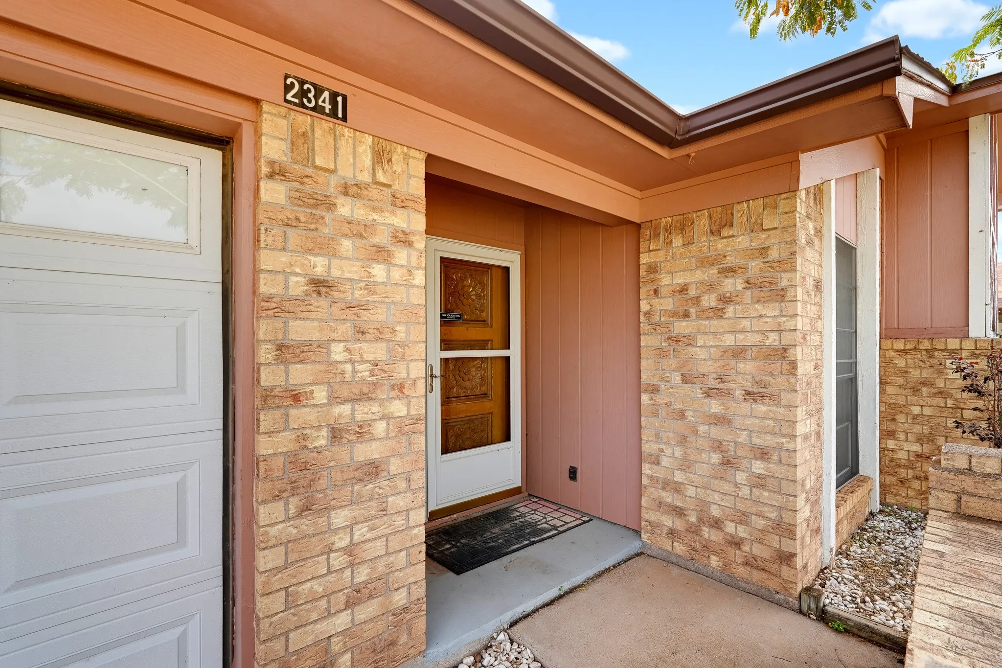 A carved wooden door, a tidy covered stoop, and warm brick framing make a welcome worth lingering over.