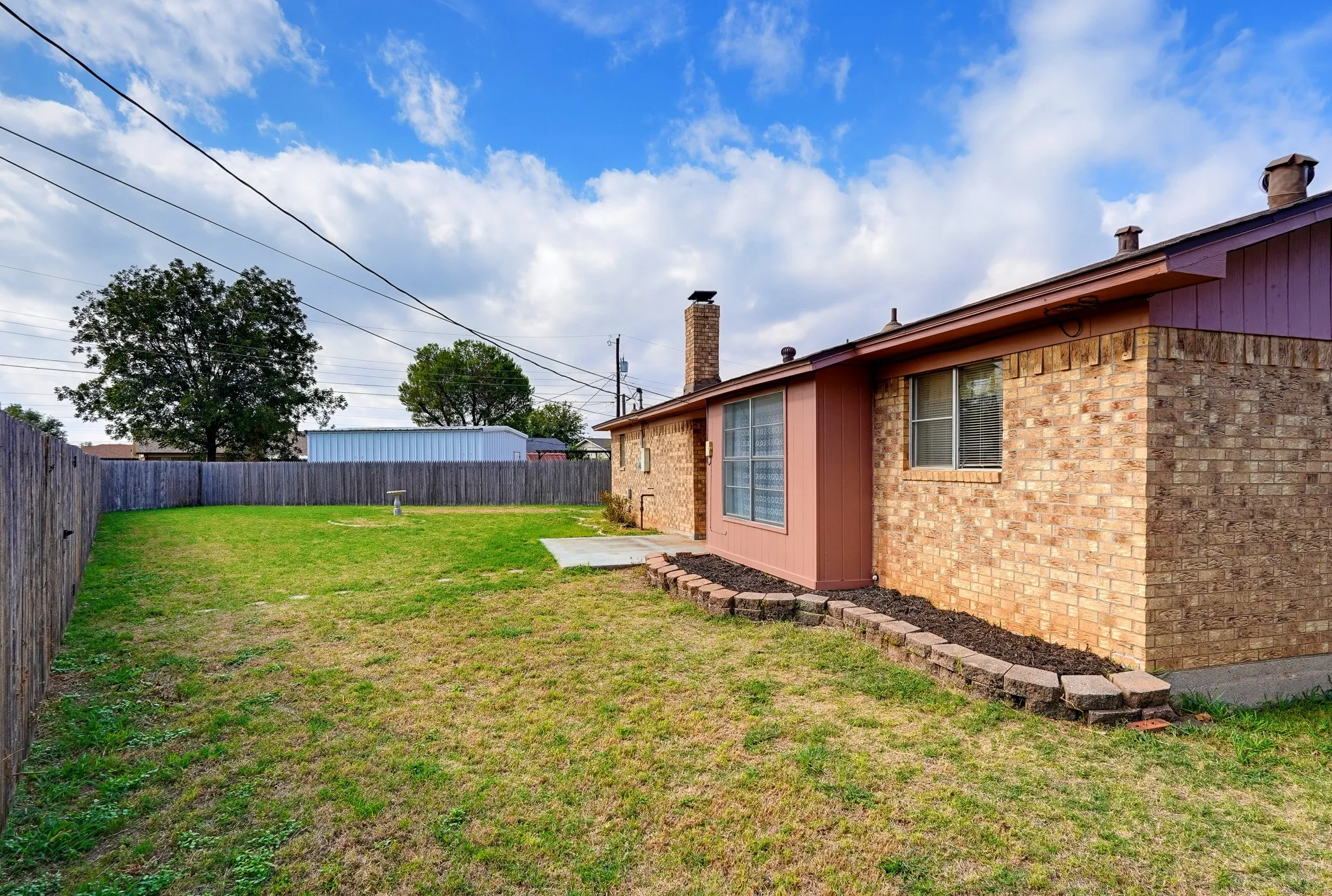 A storage building waits in the corner for mowers, bikes, and holiday decor, with a fence gate close by.