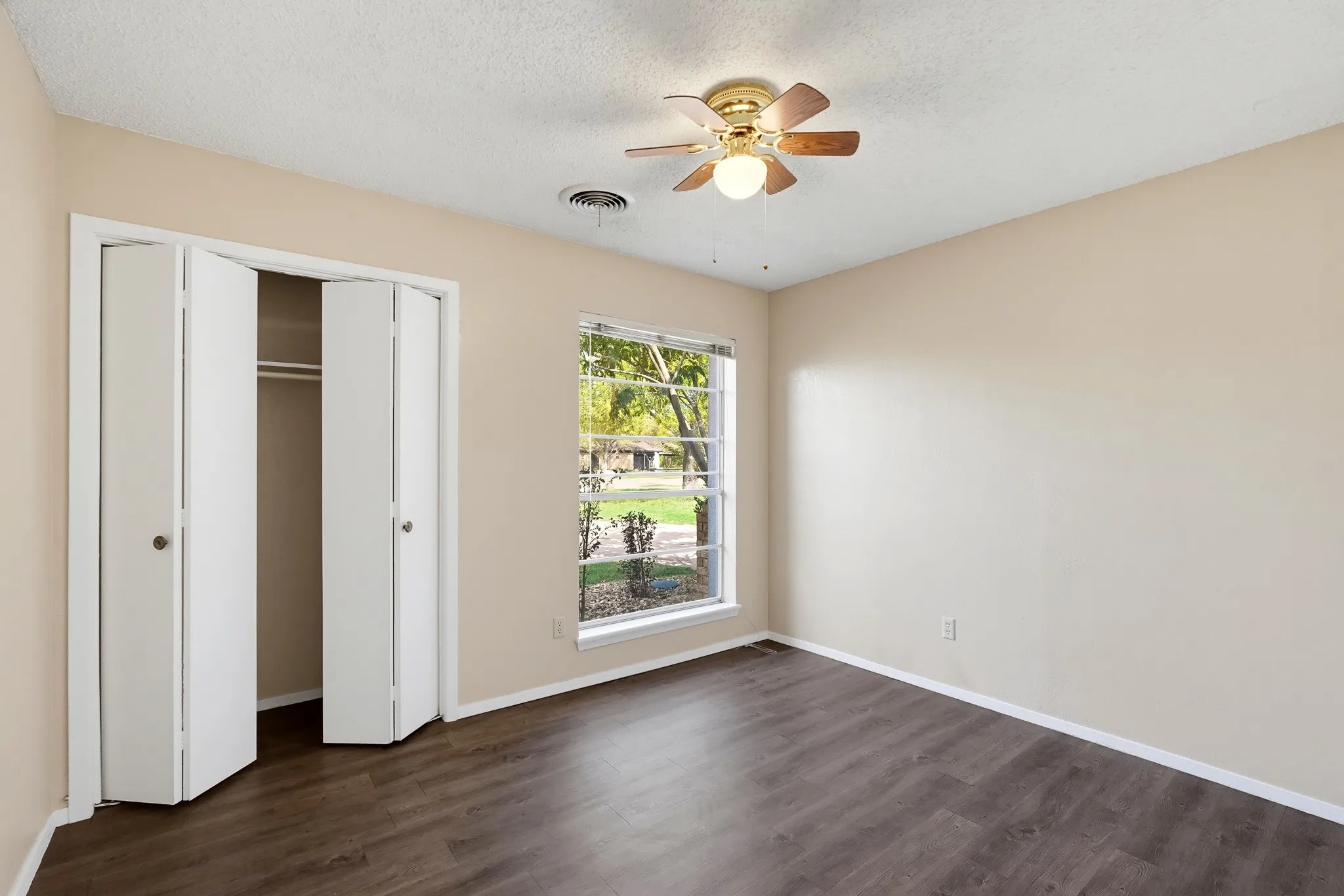 A leafy window view, a ceiling fan overhead, and a roomy closet with folding doors.