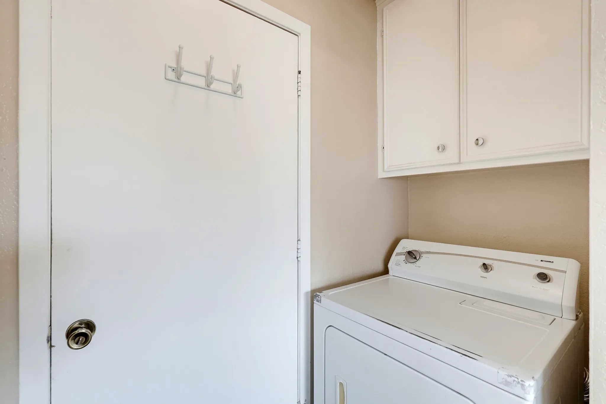 Overhead cabinets for detergent and a door with hooks for jackets and totes.