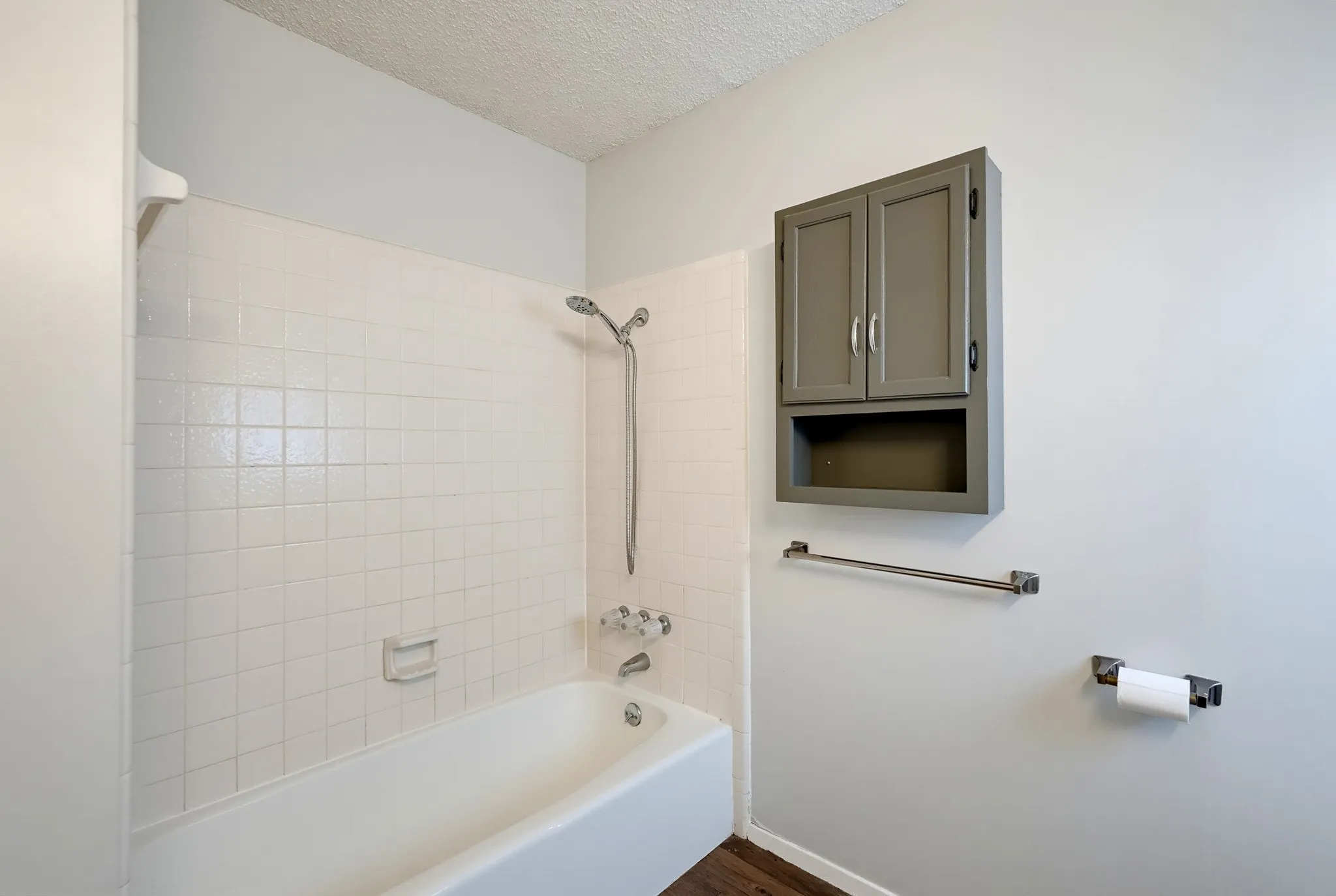 Tile surround, a handheld showerhead, and a wall cabinet for towels and toiletries.