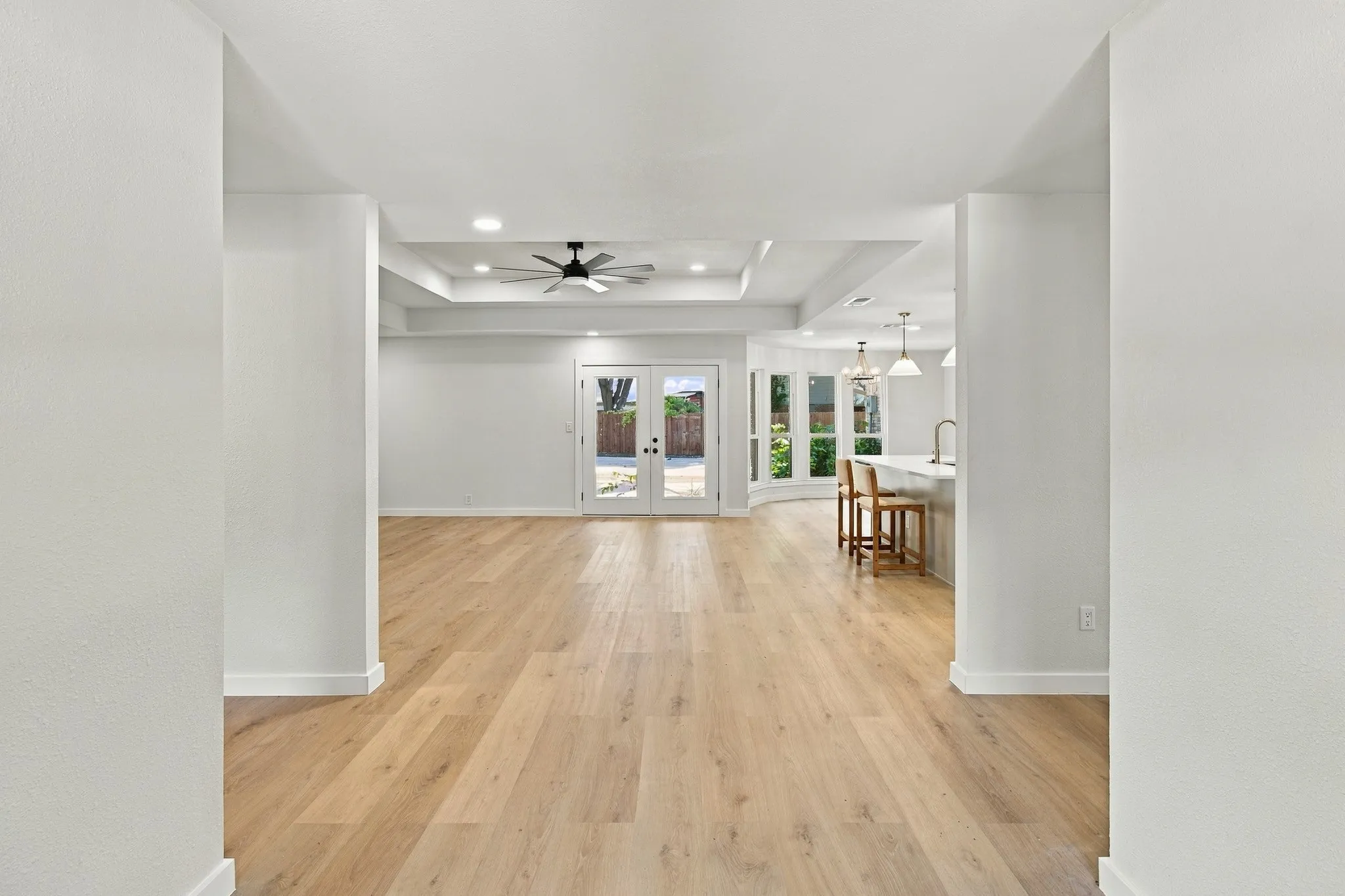 Wood-finish flooring, recessed lighting, tray ceiling with a multi-blade ceiling fan, and double glass-paned doors