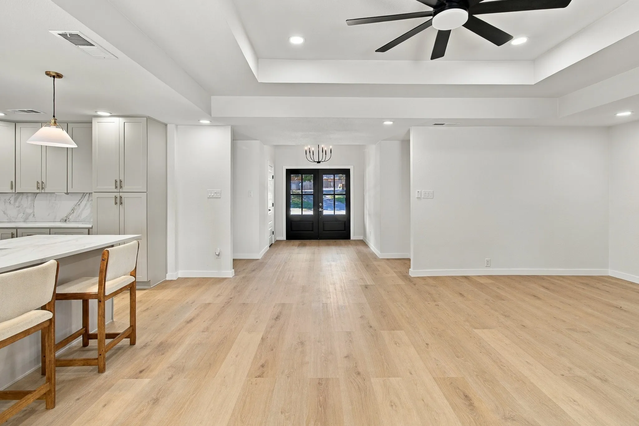 Open-concept area featuring wood-finish flooring, a tray ceiling with a multi-blade ceiling fan, recessed lighting, and double glass-paneled entry doors