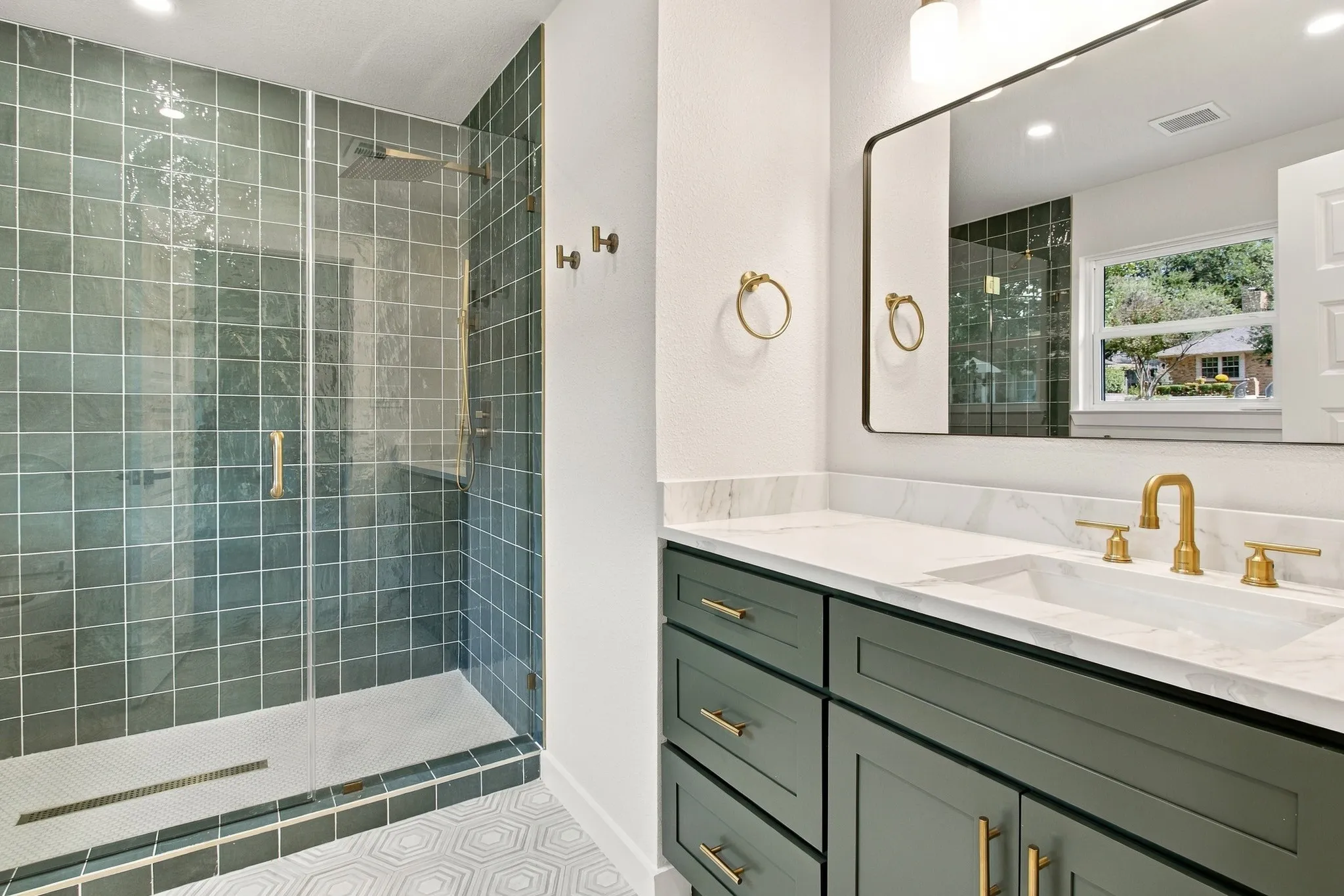 Bathroom featuring a walk-in shower with sage green square tile, vanity with stone-finish countertop, brass-tone hardware, rectangular undermount sink, and geometric patterned floor tile