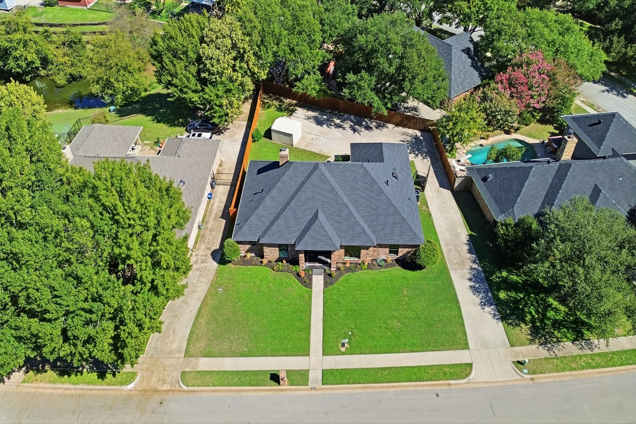 Brick exterior featuring a multi-gabled roof, mature landscaping, concrete driveway, and a detached storage structure