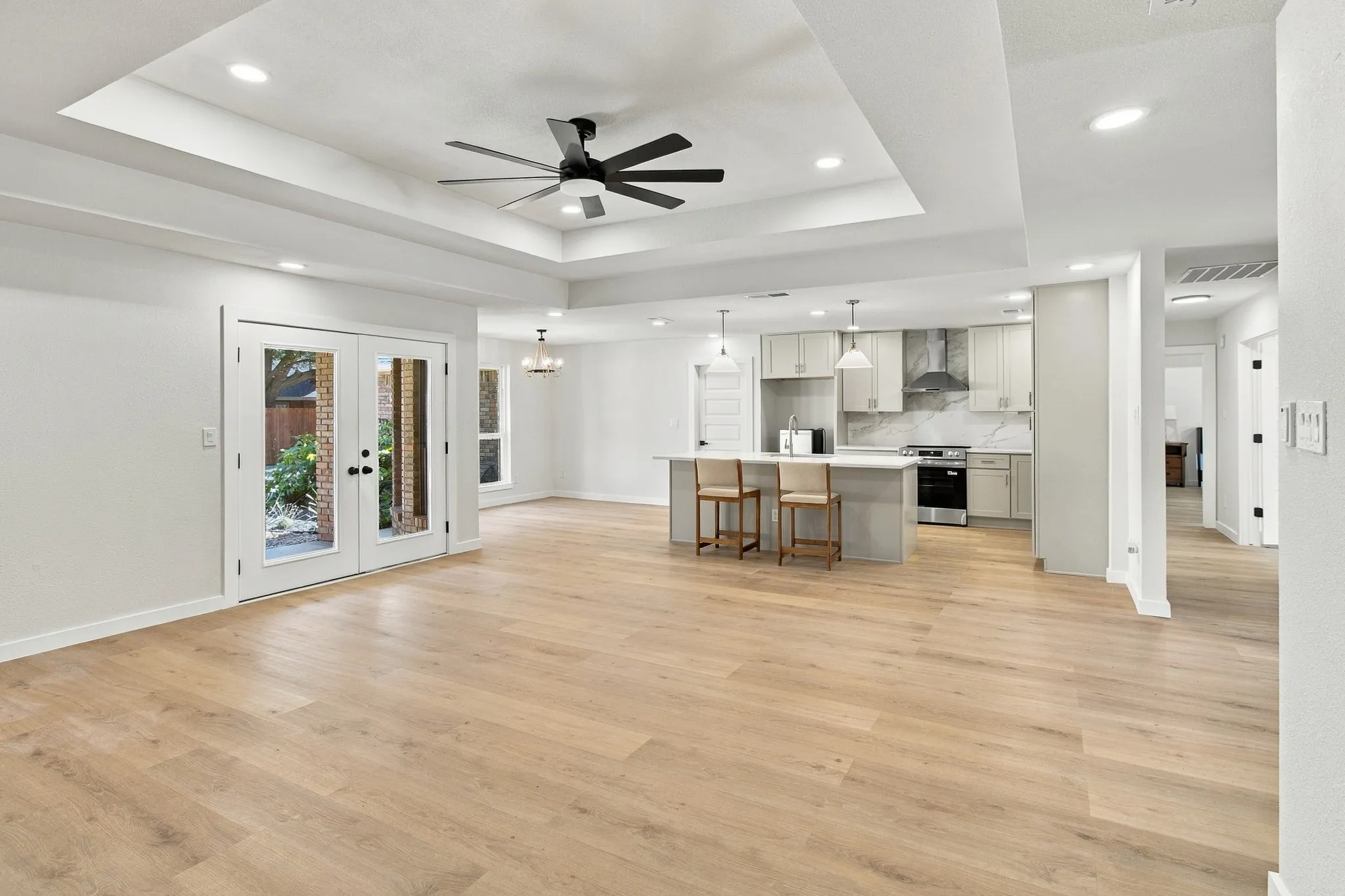 Open floor plan featuring wood-finish flooring, recessed lighting, a tray ceiling with a multi-blade ceiling fan, a center kitchen island, and French doors