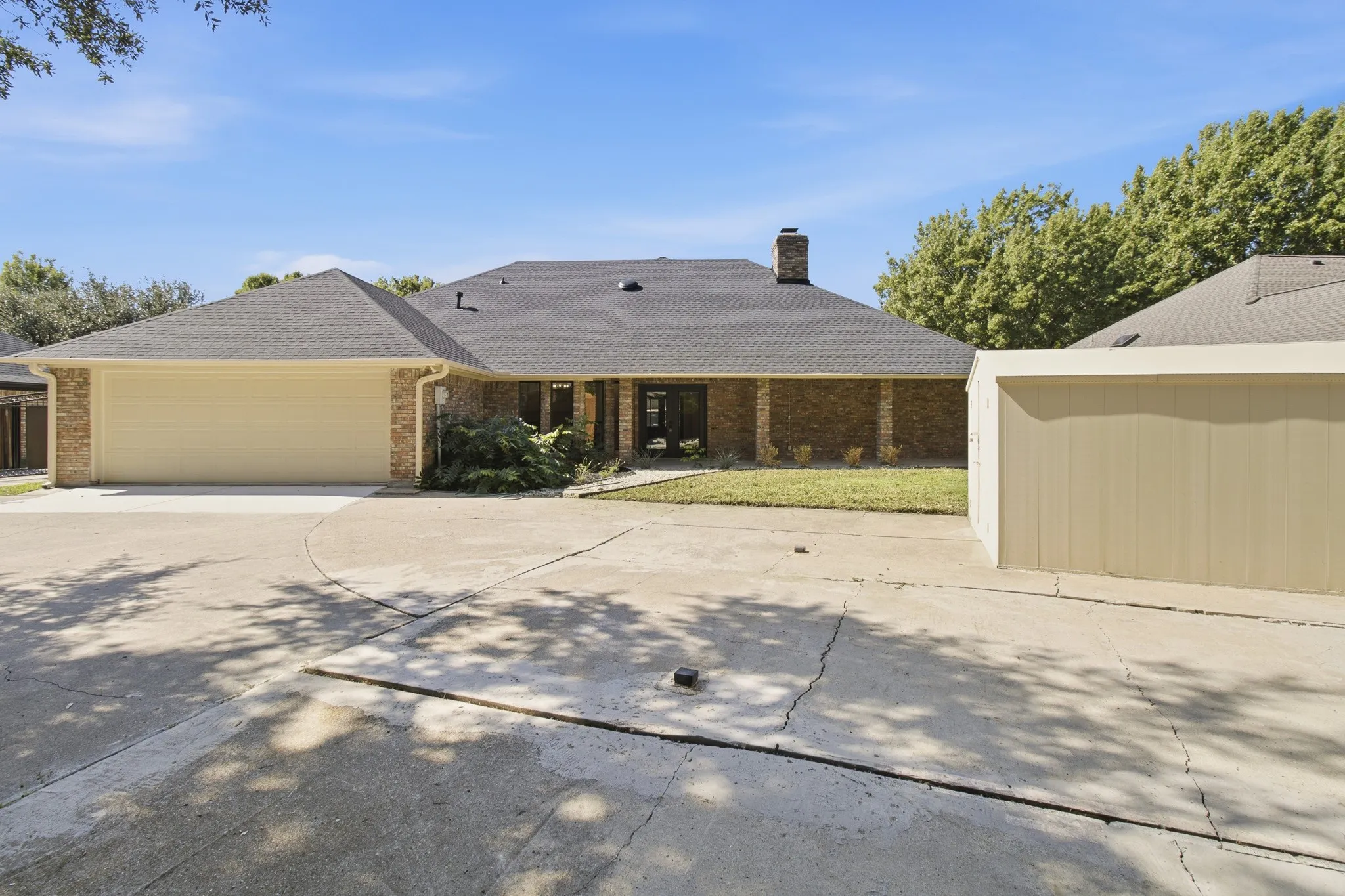 Single-story brick exterior featuring a multi-gable roofline, attached two-car garage, masonry chimney, and metal storage structure