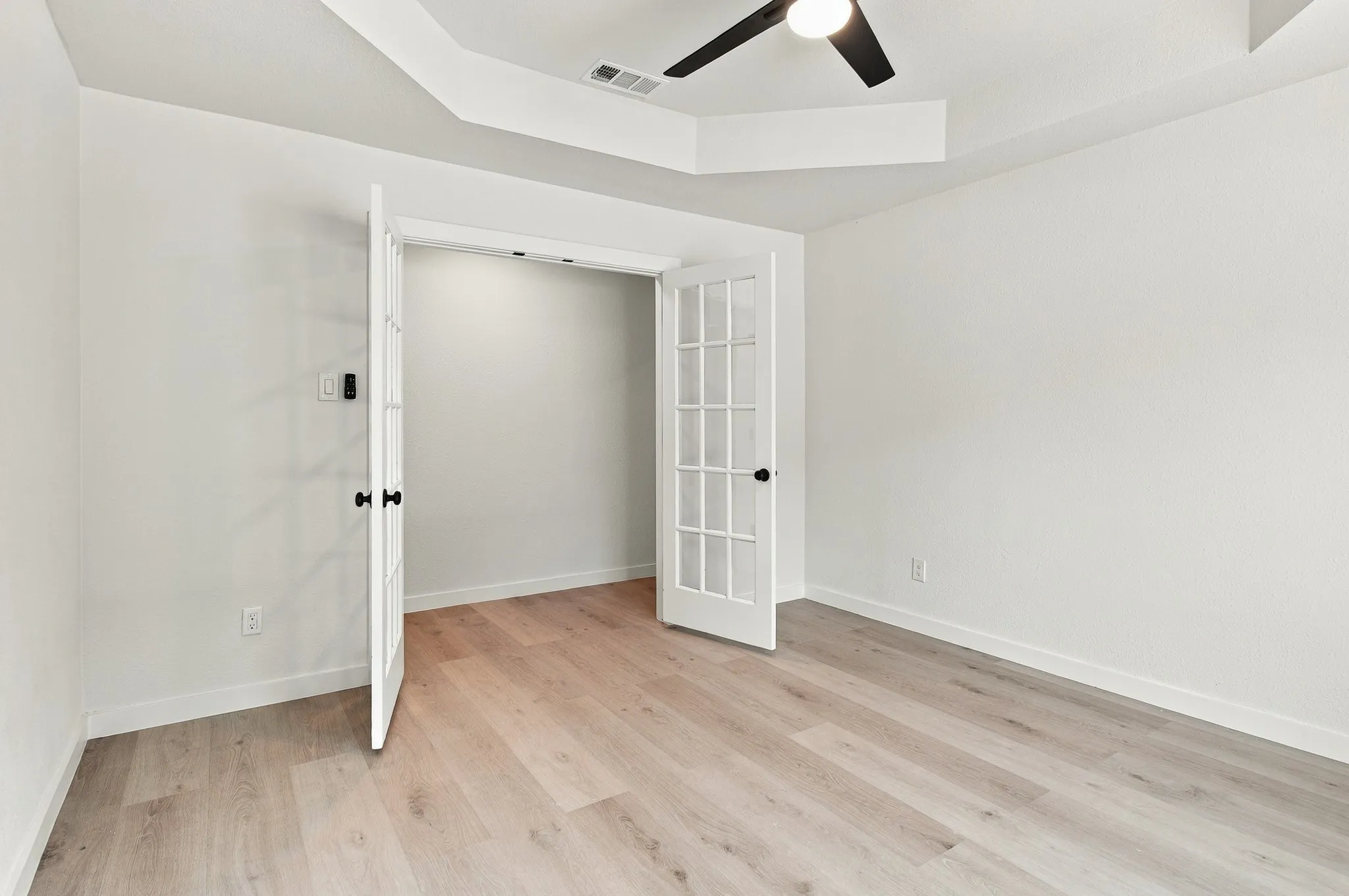 Room featuring wood-finish flooring, a tray ceiling with a matte black ceiling fan, and double French doors with glass panes
