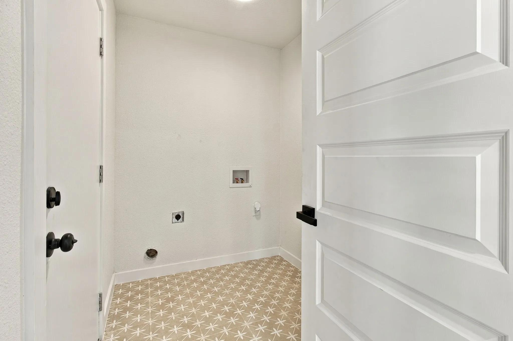 Utility area featuring patterned tile flooring, a four-panel interior door, and matte black hardware