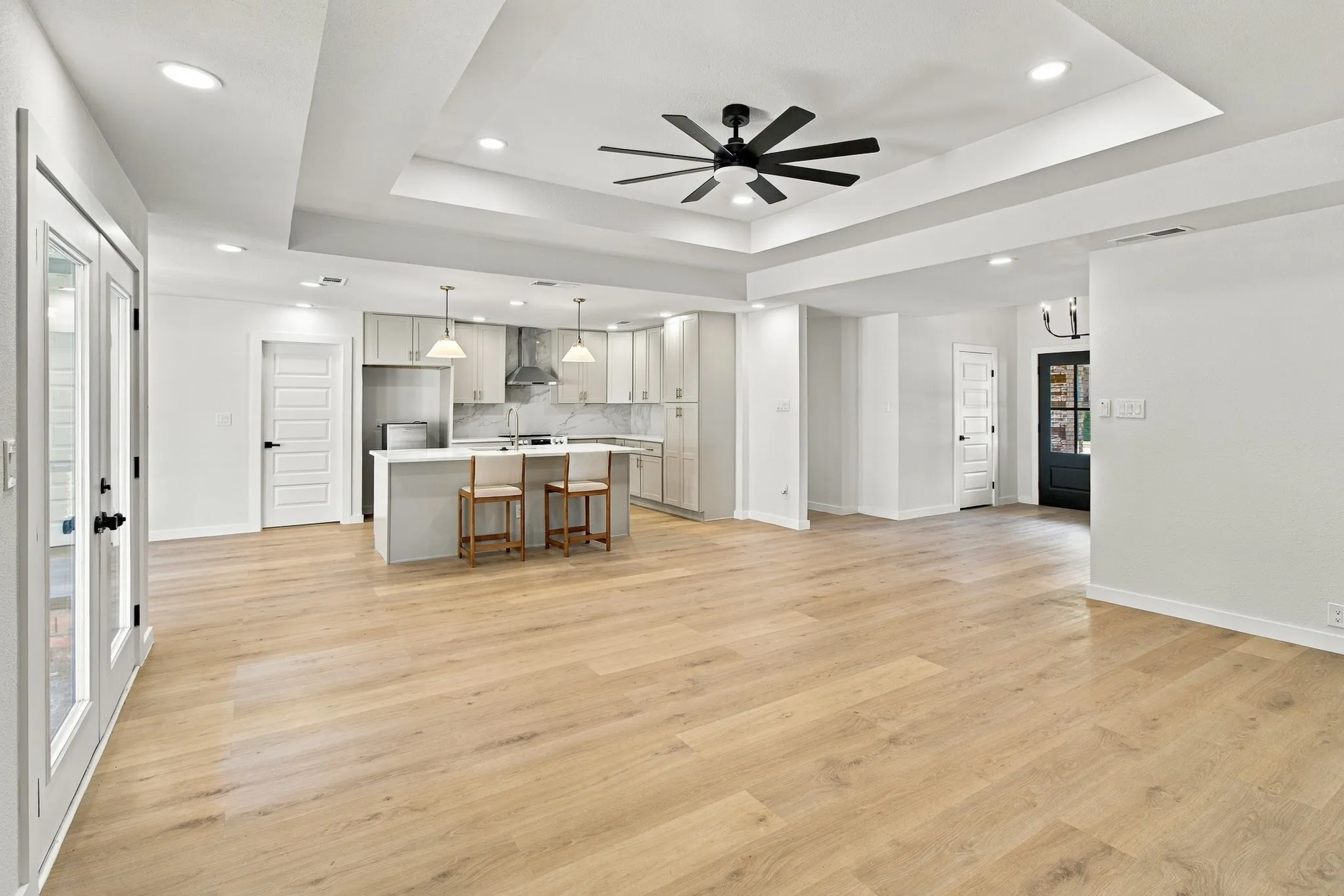 Tray ceiling with recessed lighting, wood-finish flooring, central kitchen island, matte black ceiling fan, and Shaker-style cabinetry