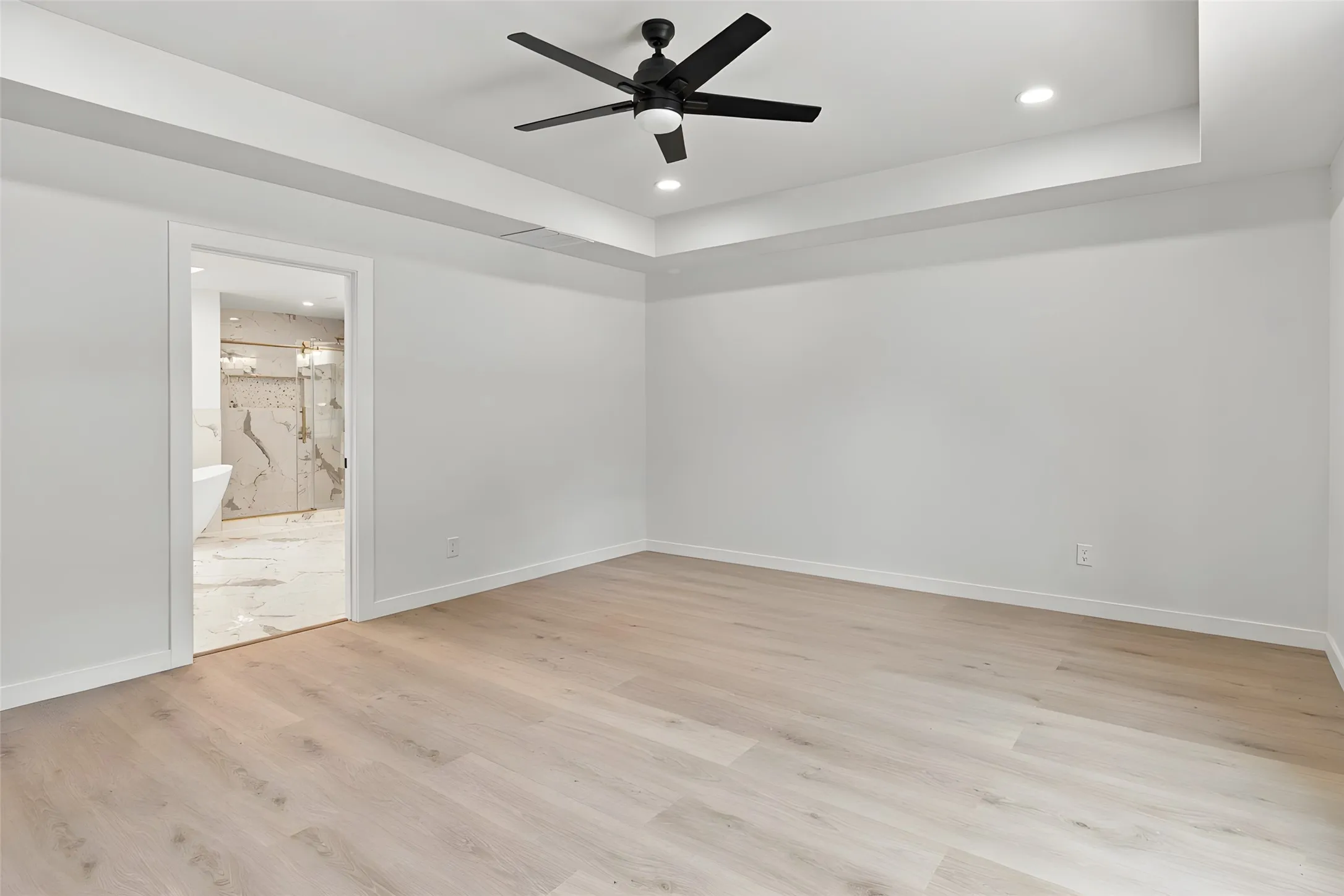 Tray ceiling featuring a central matte black ceiling fan, recessed lighting, and wood-finish flooring