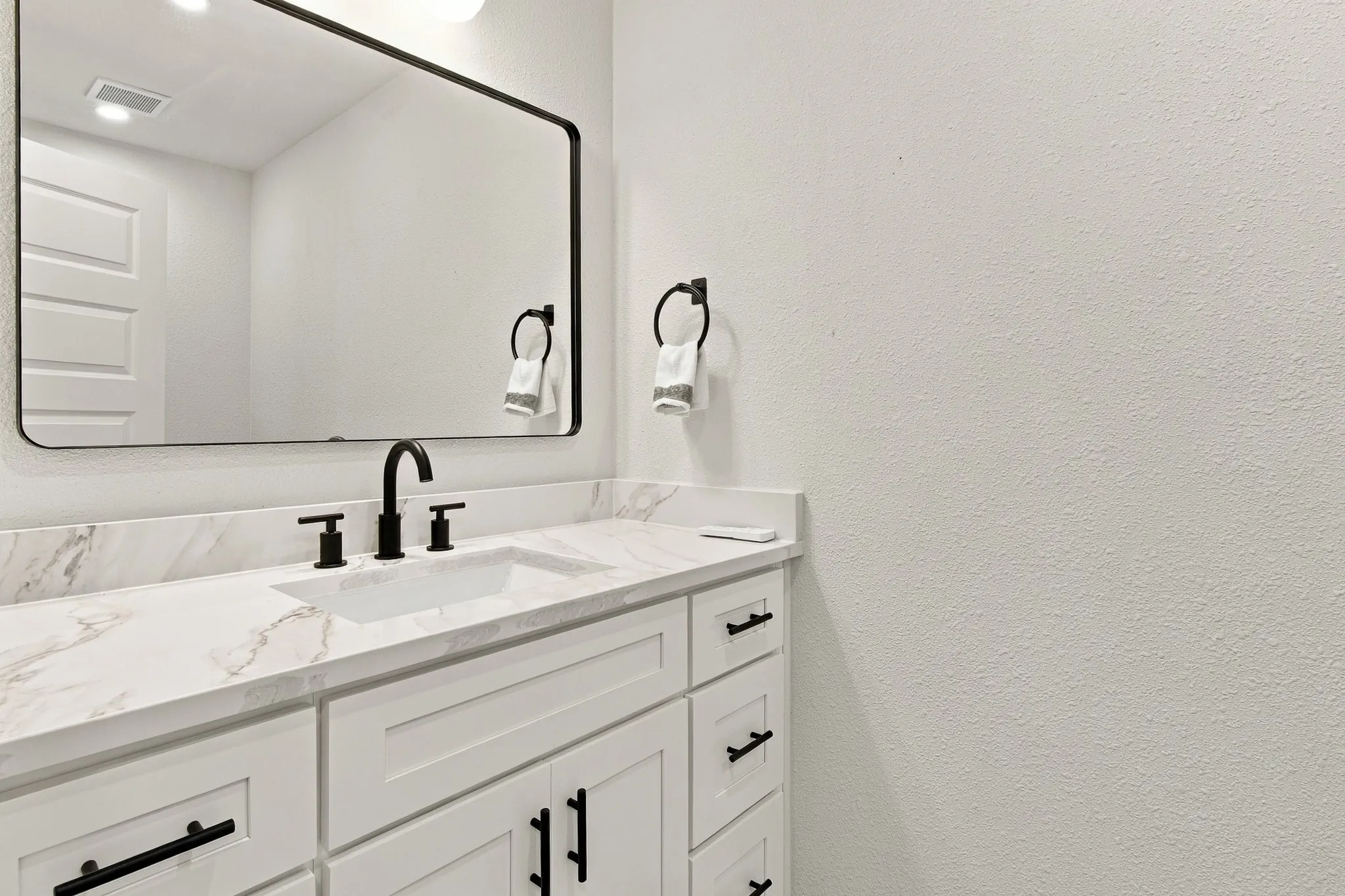 Vanity featuring a stone-look countertop, undermount sink, matte black faucet, and cabinetry with matte black hardware, accented by a matching framed mirror