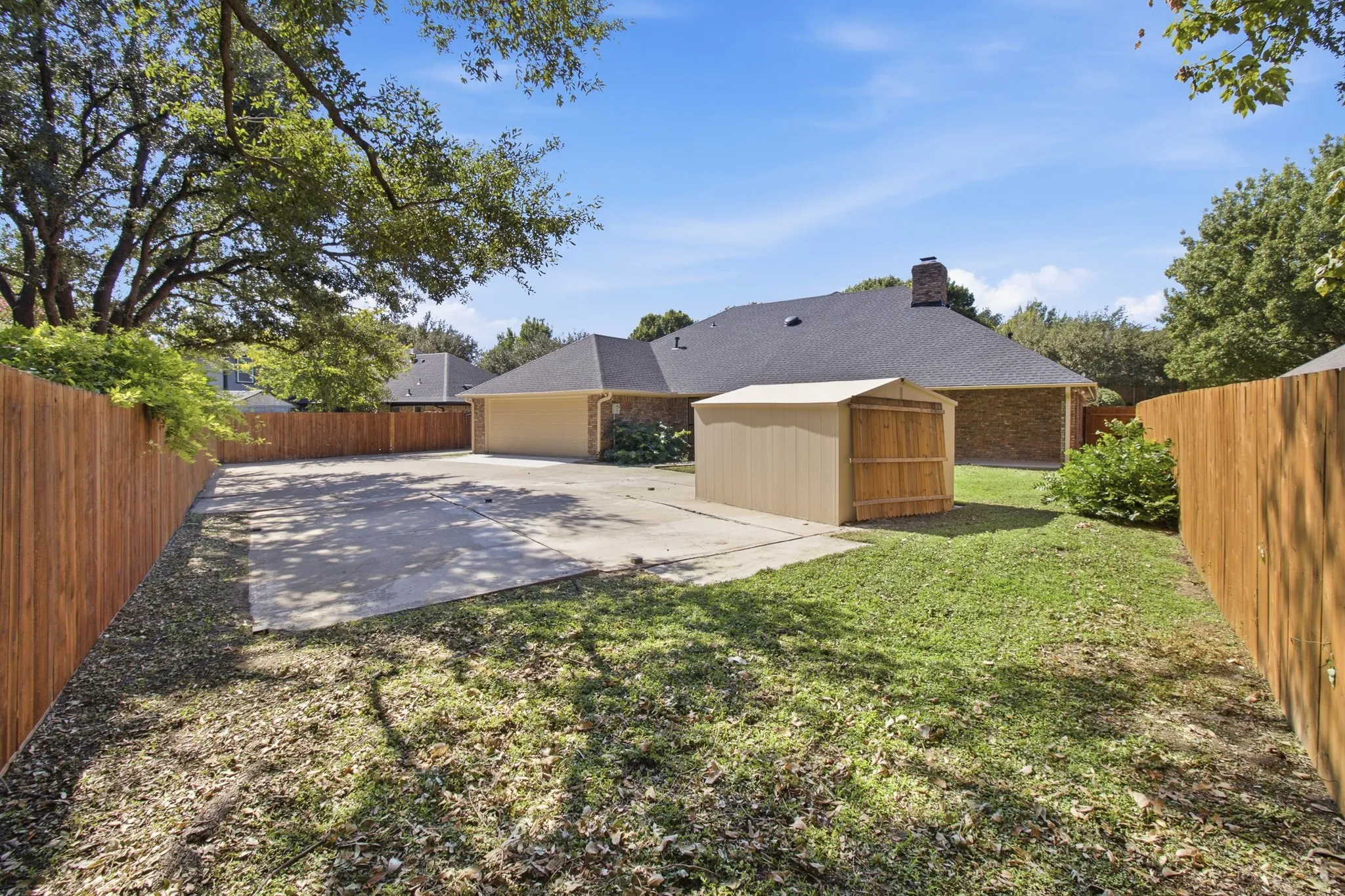 Exterior space featuring a concrete parking pad, wood privacy fencing, mature trees, and a detached metal storage structure