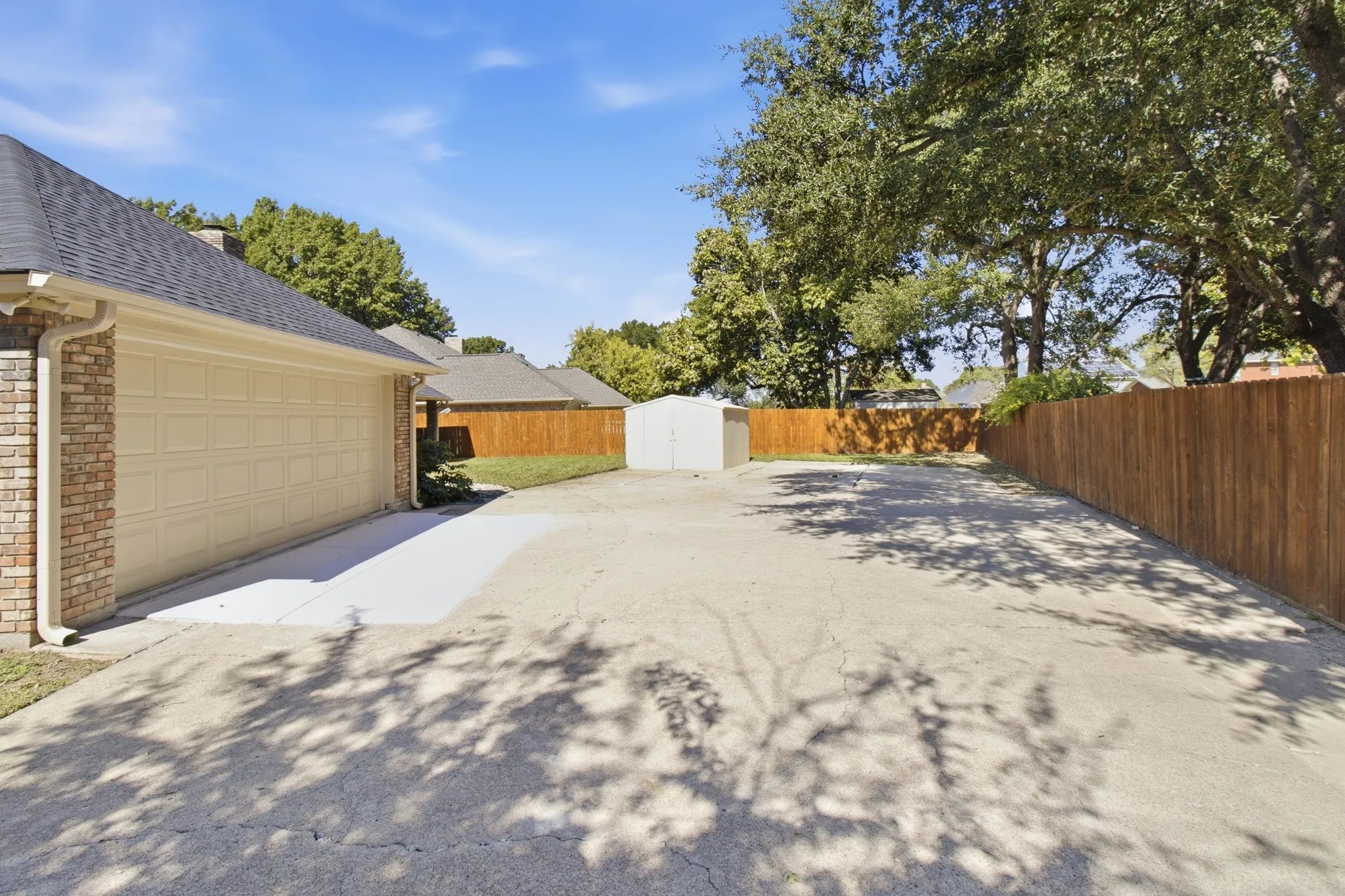 Expansive paved driveway with attached two-car garage, perimeter wood fencing, and freestanding storage shed