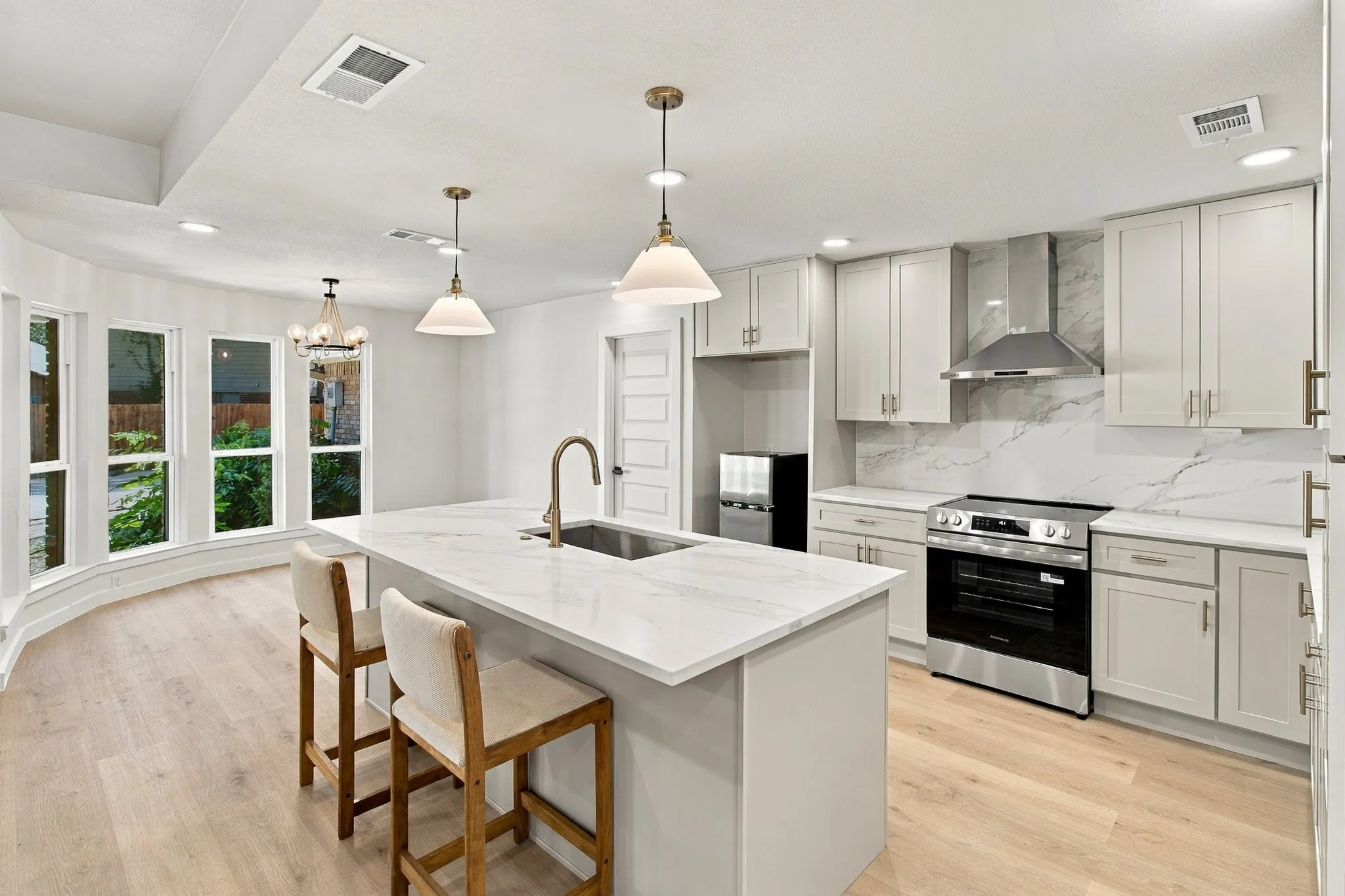 Kitchen featuring light-toned cabinetry, stone-finish countertops, stainless steel appliances, a center island with an integrated sink, and wood-finish flooring