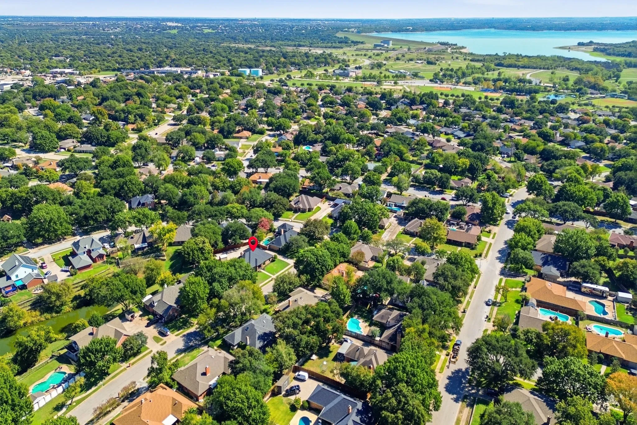 Aerial perspective showcasing a mature, tree-lined neighborhood situated in proximity to a large reservoir