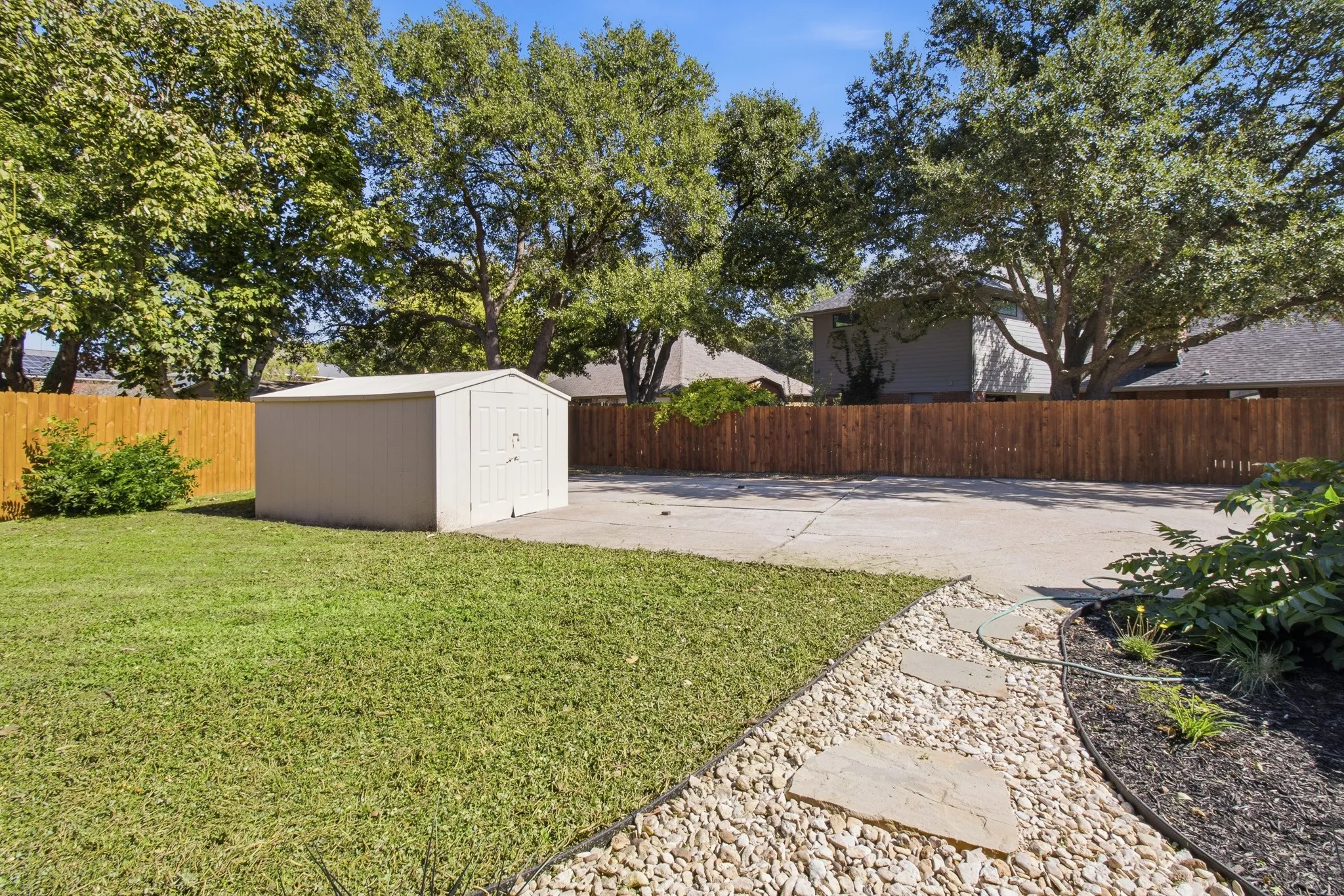 Backyard featuring a concrete pad, detached storage structure, wooden privacy fencing, natural stone pathing, and mature trees