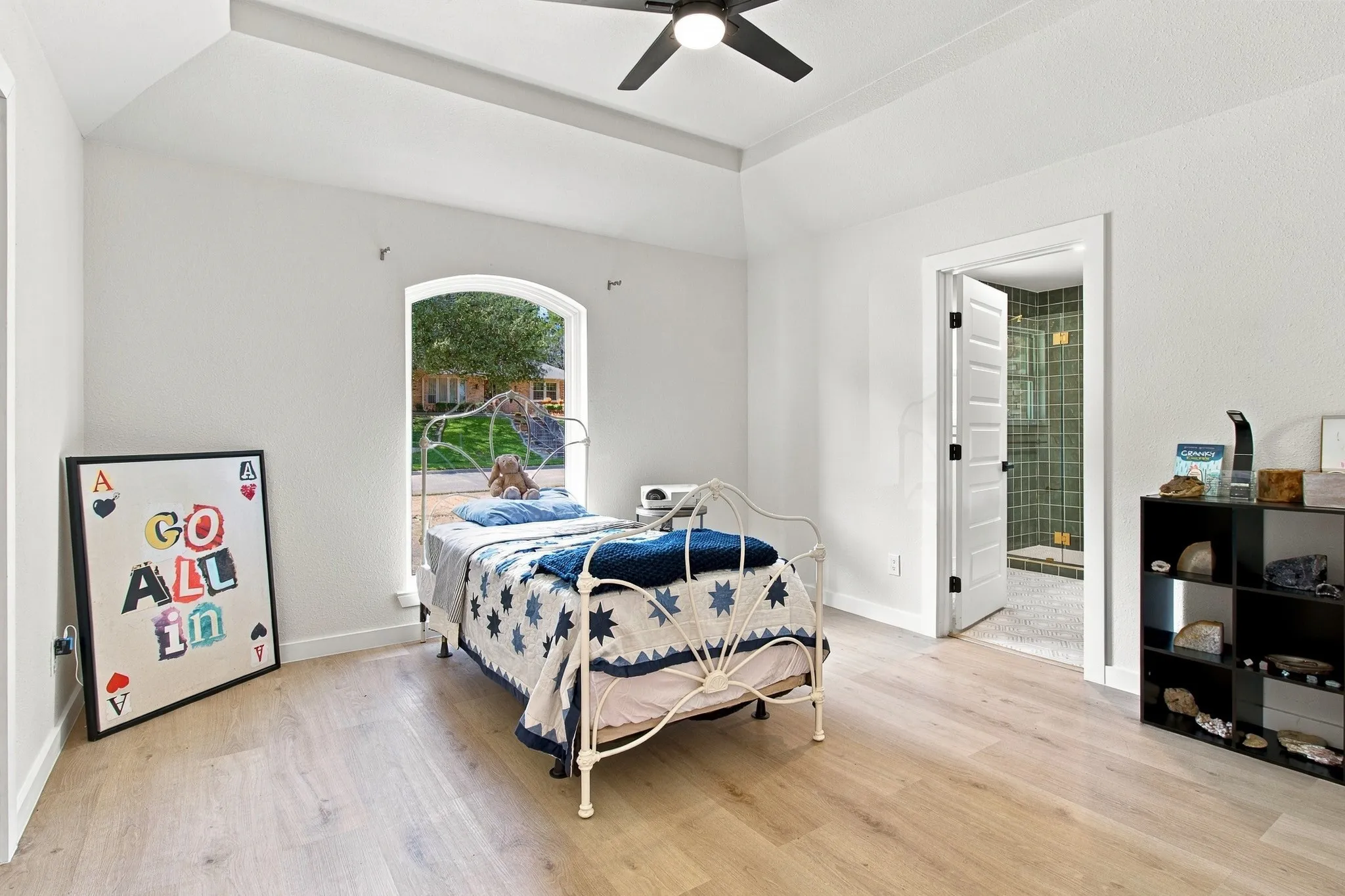 Bedroom featuring wood-finish flooring, tray ceiling with a central ceiling fan, and an arched window
