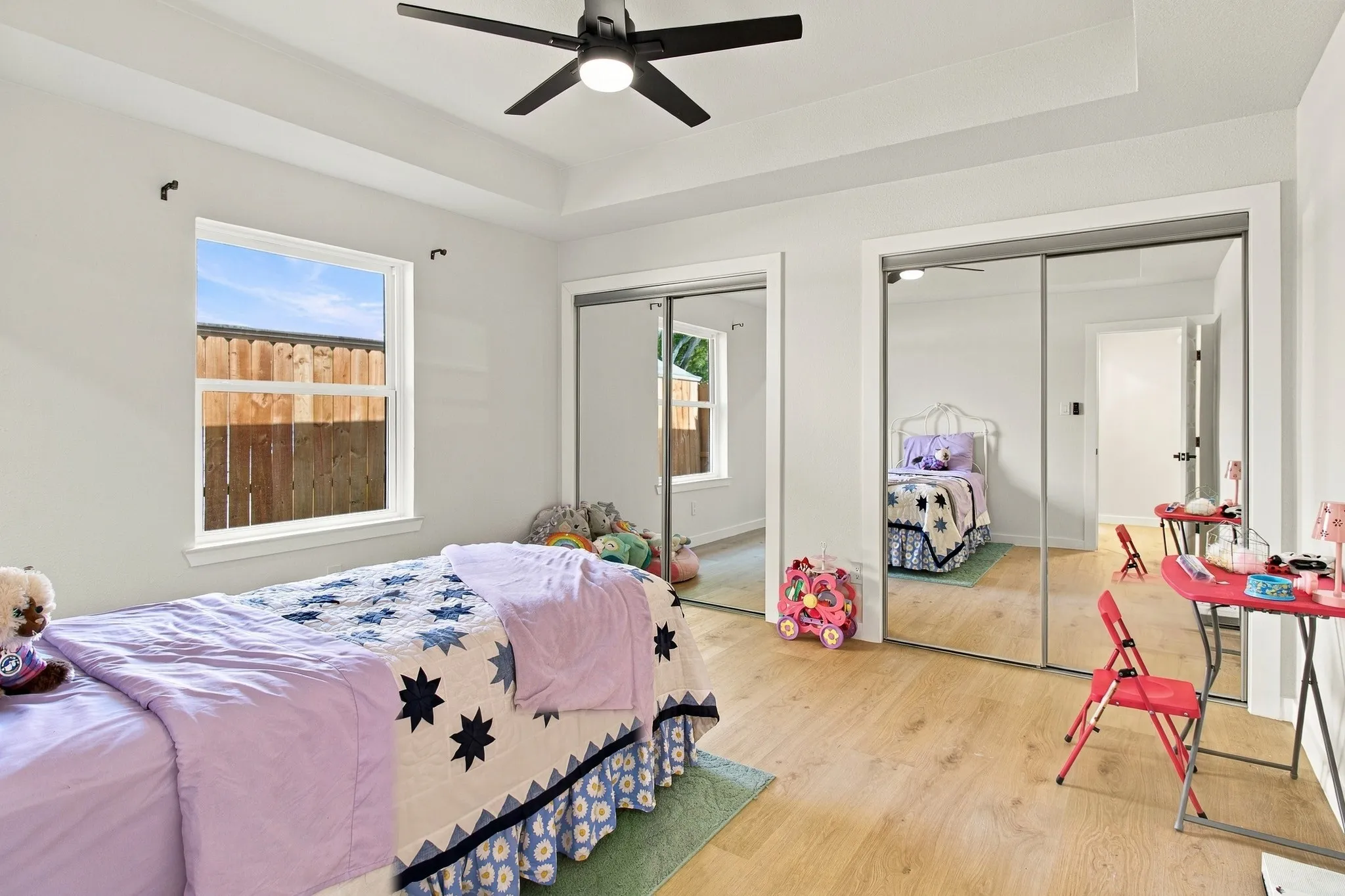 Tray ceiling, wood-finish flooring, dual mirrored sliding-door closets, and a centrally mounted ceiling fan