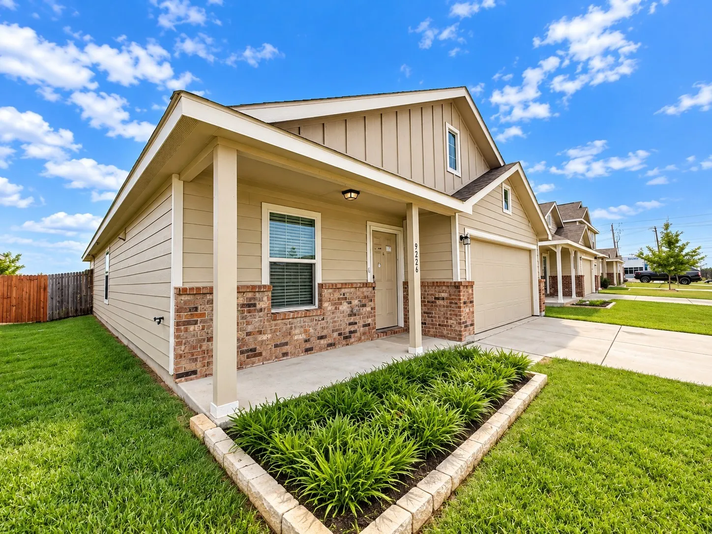 Siding exterior with brick accents, covered front porch, attached garage, and a landscaped front yard with a planting bed