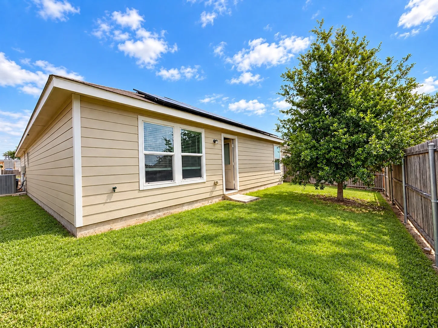 Expansive backyard featuring a manicured lawn, established tree, and wood privacy fencing