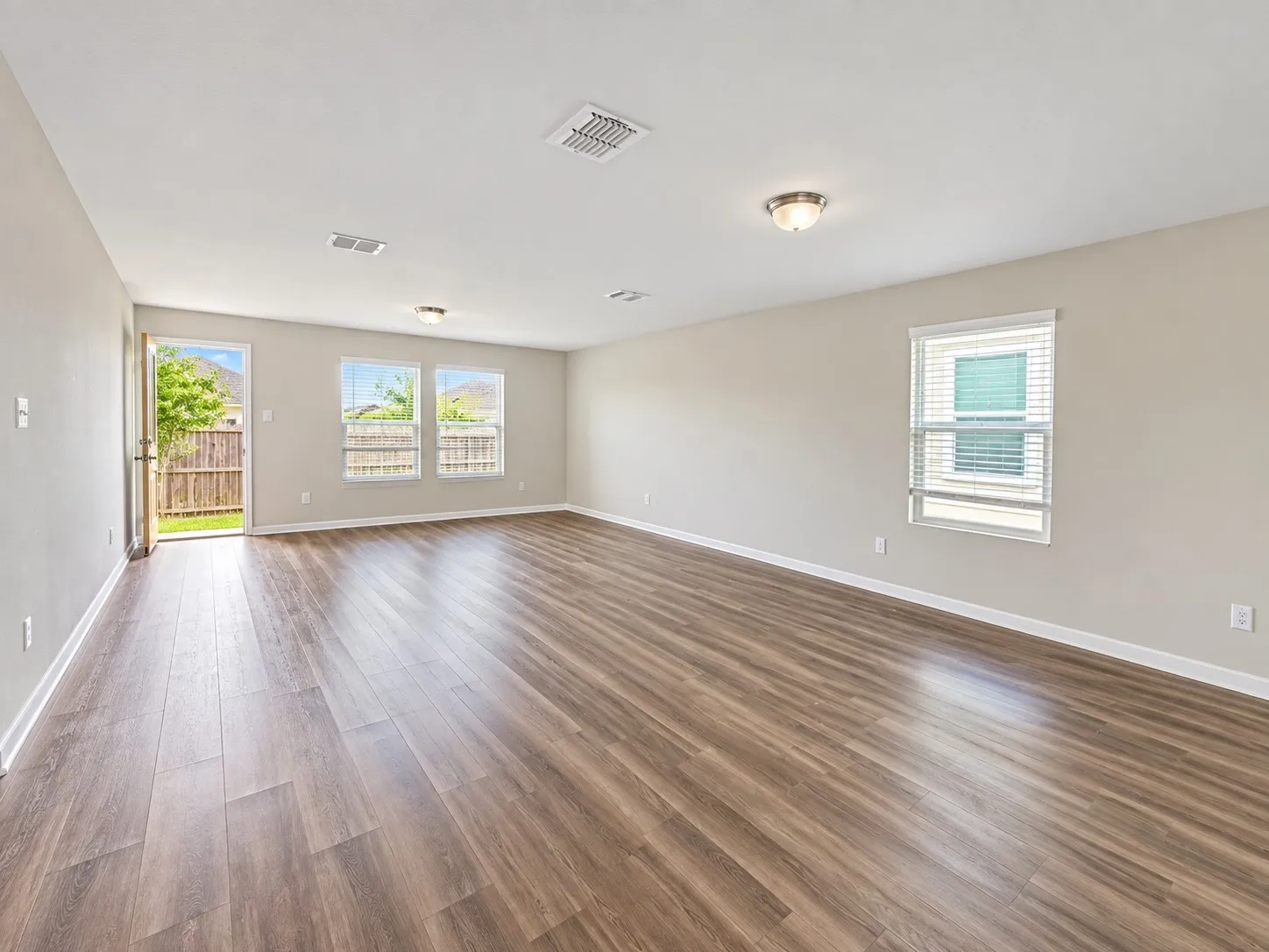 Wood-finish flooring, multiple windows with blinds, recessed lighting, and a rear exterior door