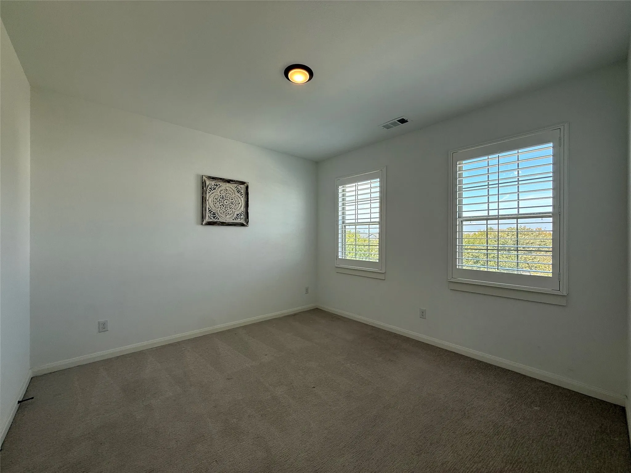Neutral-toned wall-to-wall carpeting, dual windows with plantation shutters, and flush-mount ceiling lighting