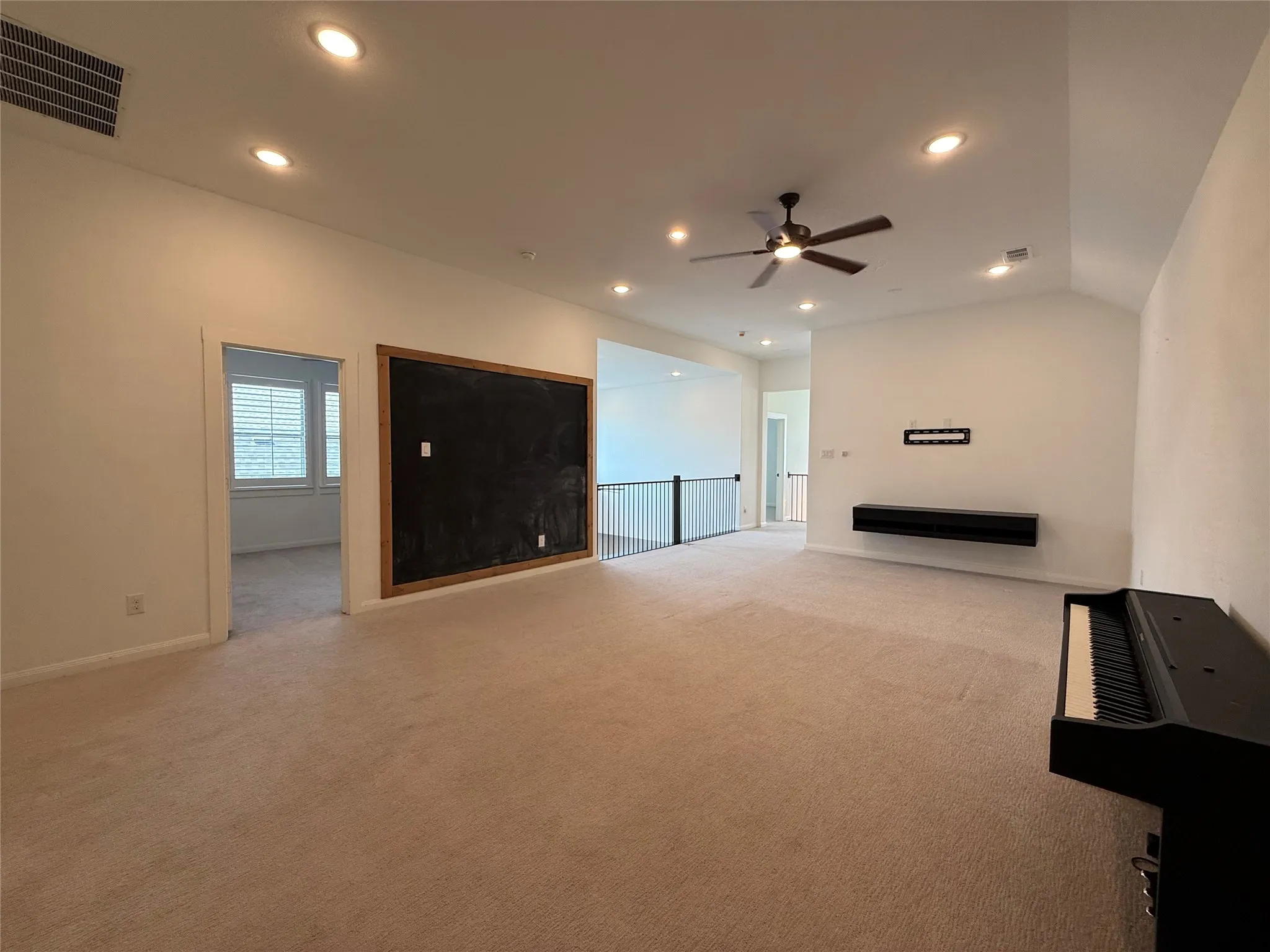 Vaulted ceilings with recessed lighting, integrated wall-mounted cabinetry, ceiling fan, and metal baluster railing