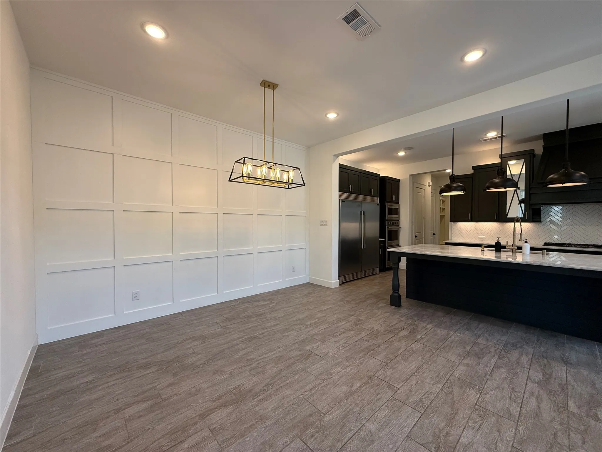 Grid-pattern wainscoting, wood-finish flooring, recessed lighting, rectangular chandelier, and a kitchen island with a stone countertop
