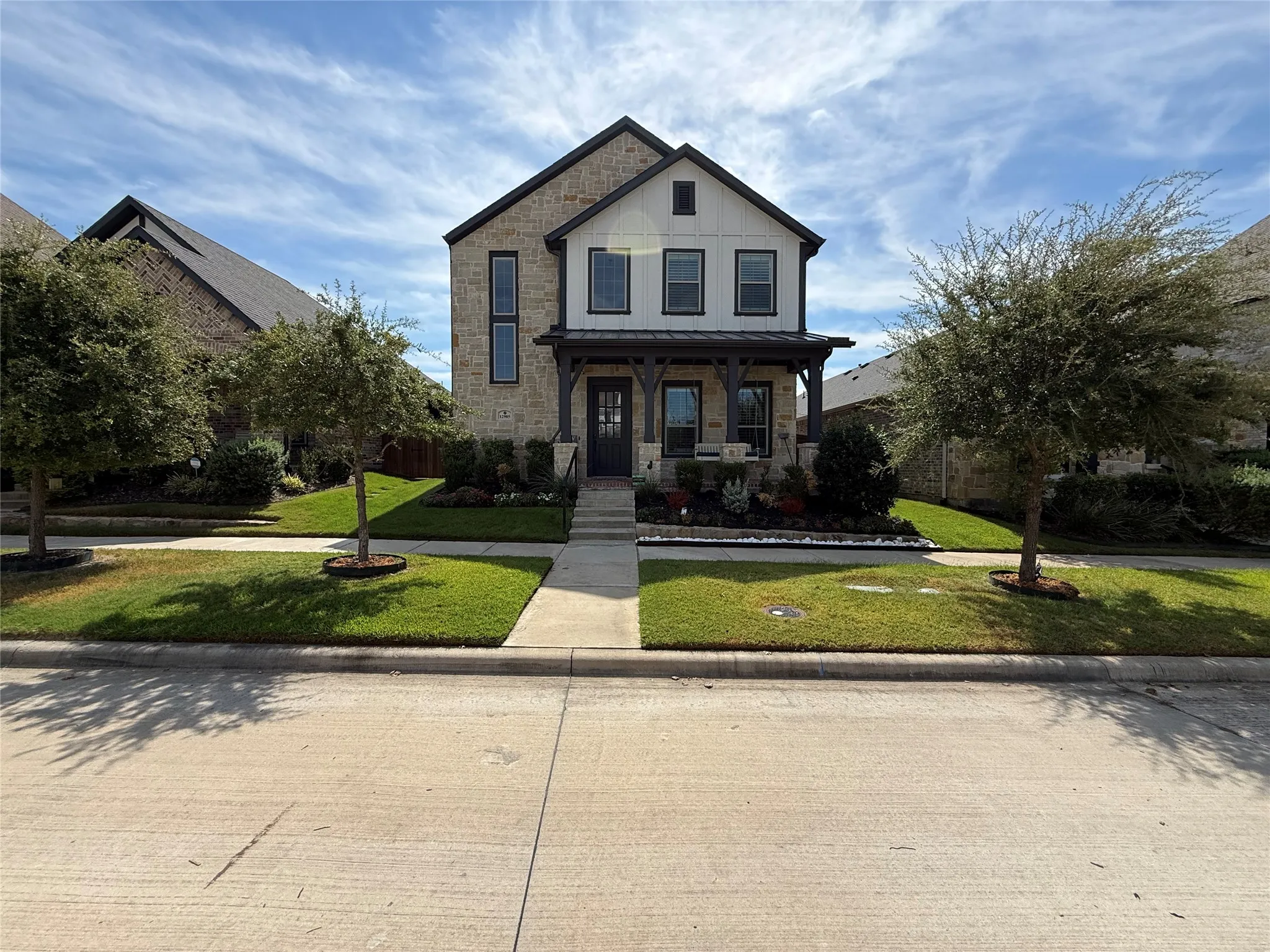 Two-story exterior featuring a stone and siding facade, a covered front porch with timber-style posts, a multi-gabled roofline, and a manicured front lawn