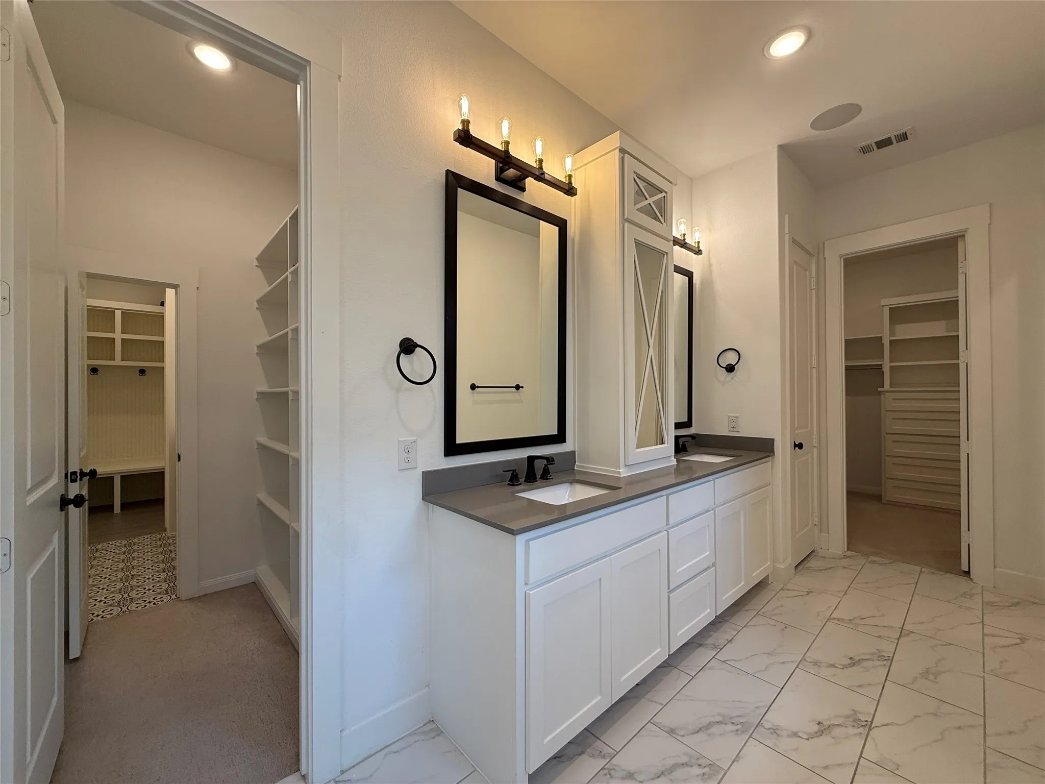 Double vanity with quartz countertops, custom white cabinetry, black hardware, and large-format tiled flooring