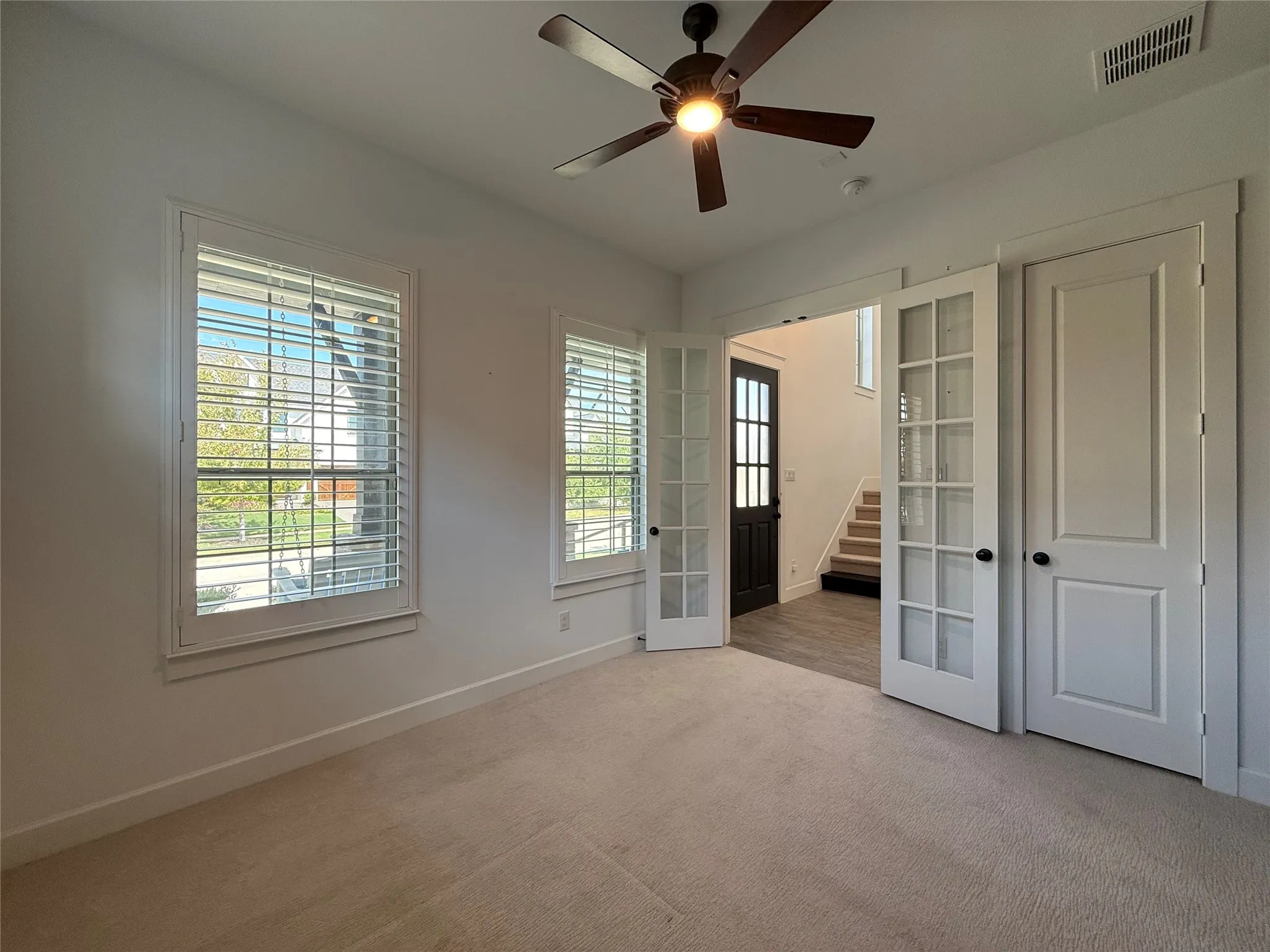 Room featuring plantation shutters, neutral carpeting, a ceiling fan with integrated lighting, and French doors